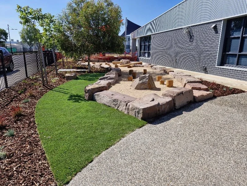 Primary school playspace rock edging synthetic turf log steppers natural wooden log play