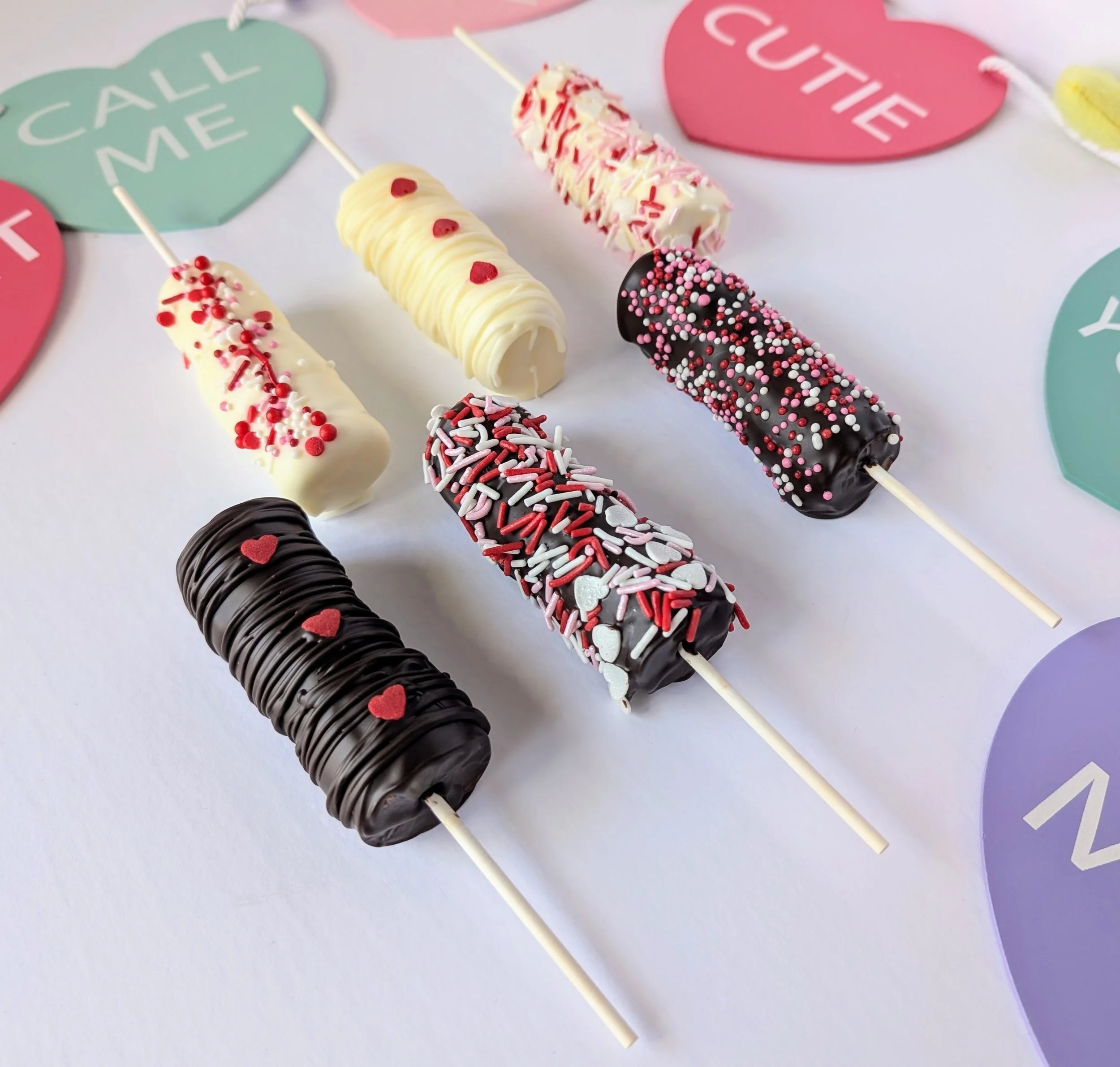 Marshmallows on a stick covered in dark chocolate, milk chocolate, and white chocolate and adorned with different kinds of sprinkles. 