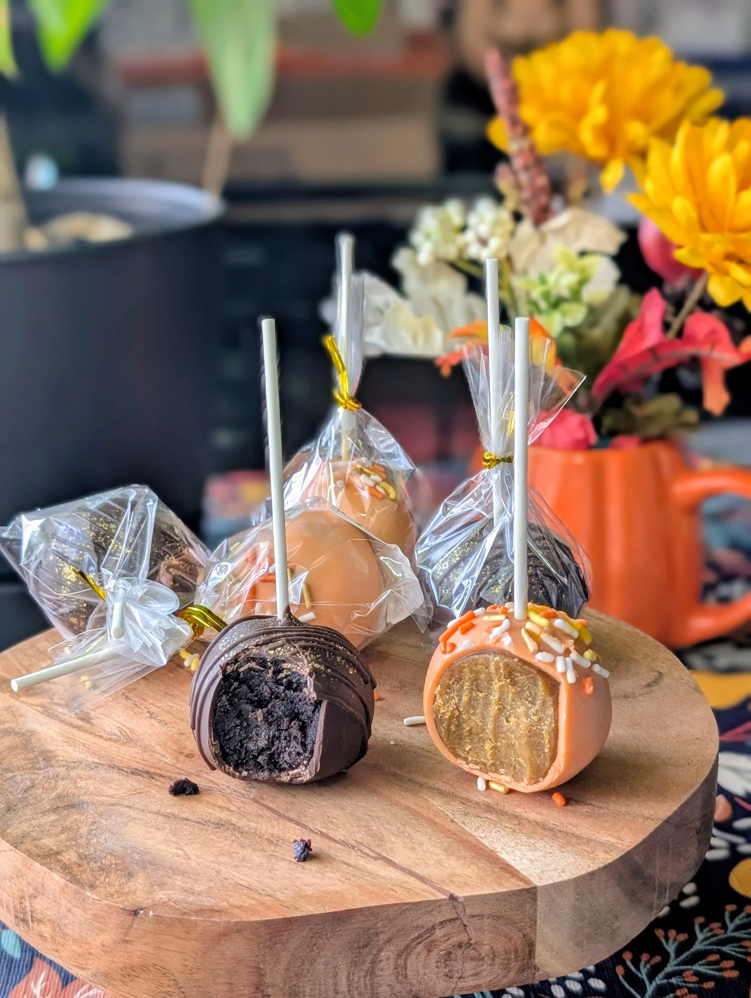 Chocolate and pumpkin spice cake pops on a wooden stand, featuring two bitten pops in front showing their dark chocolate and pumpkin interiors.