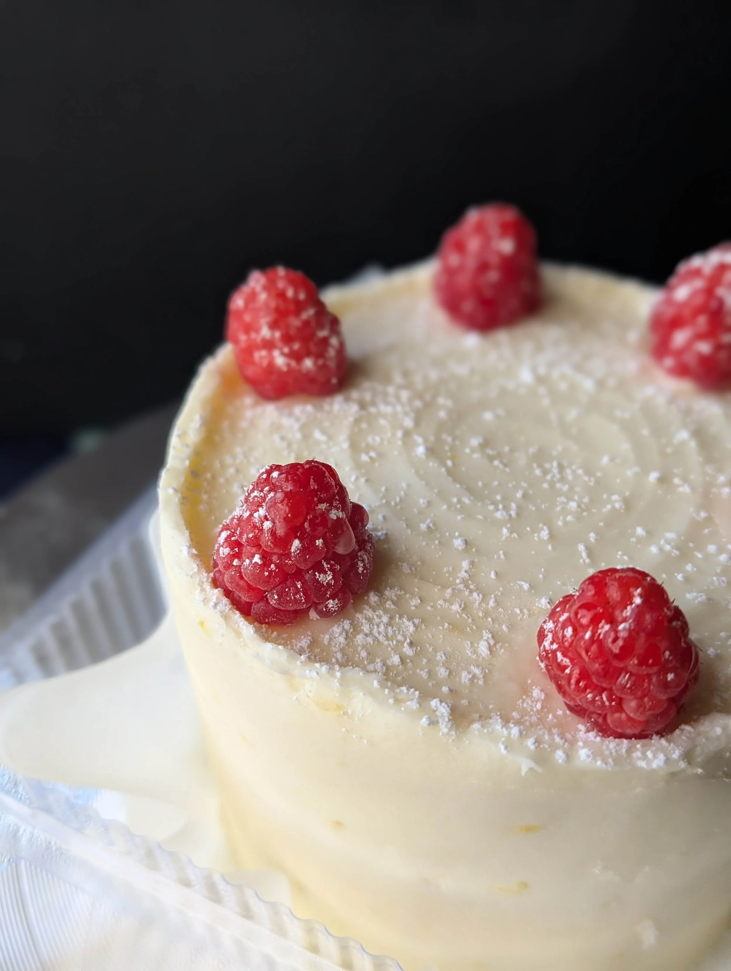 Close-up of a white cream cake decorated with fresh raspberries and powdered sugar on top.
