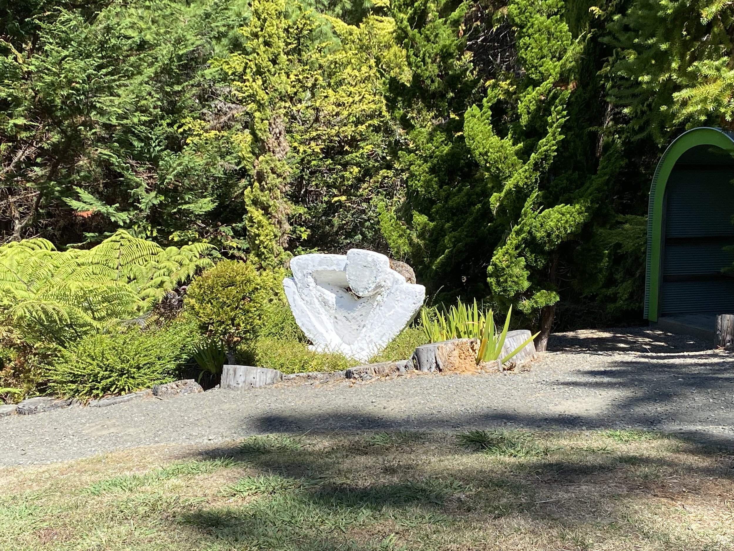White sculptural artwork in a garden surrounded by trees and plants.