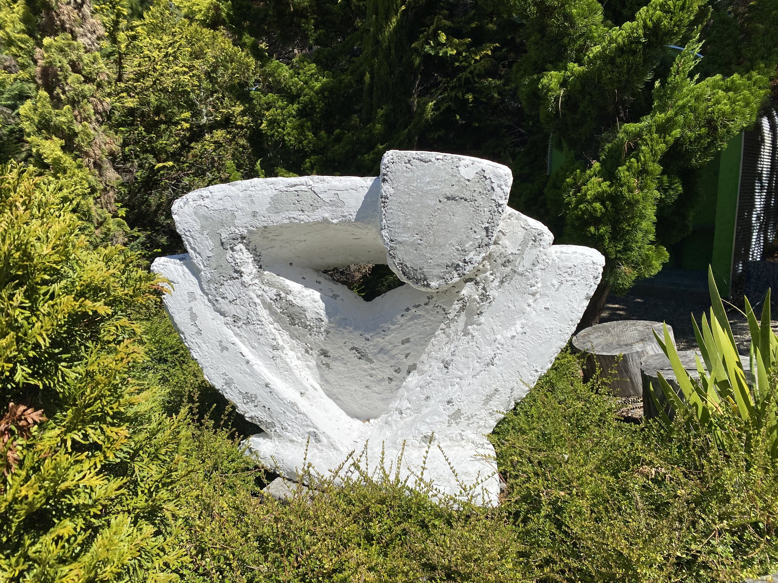 Abstract white sculpture in a garden surrounded by greenery.