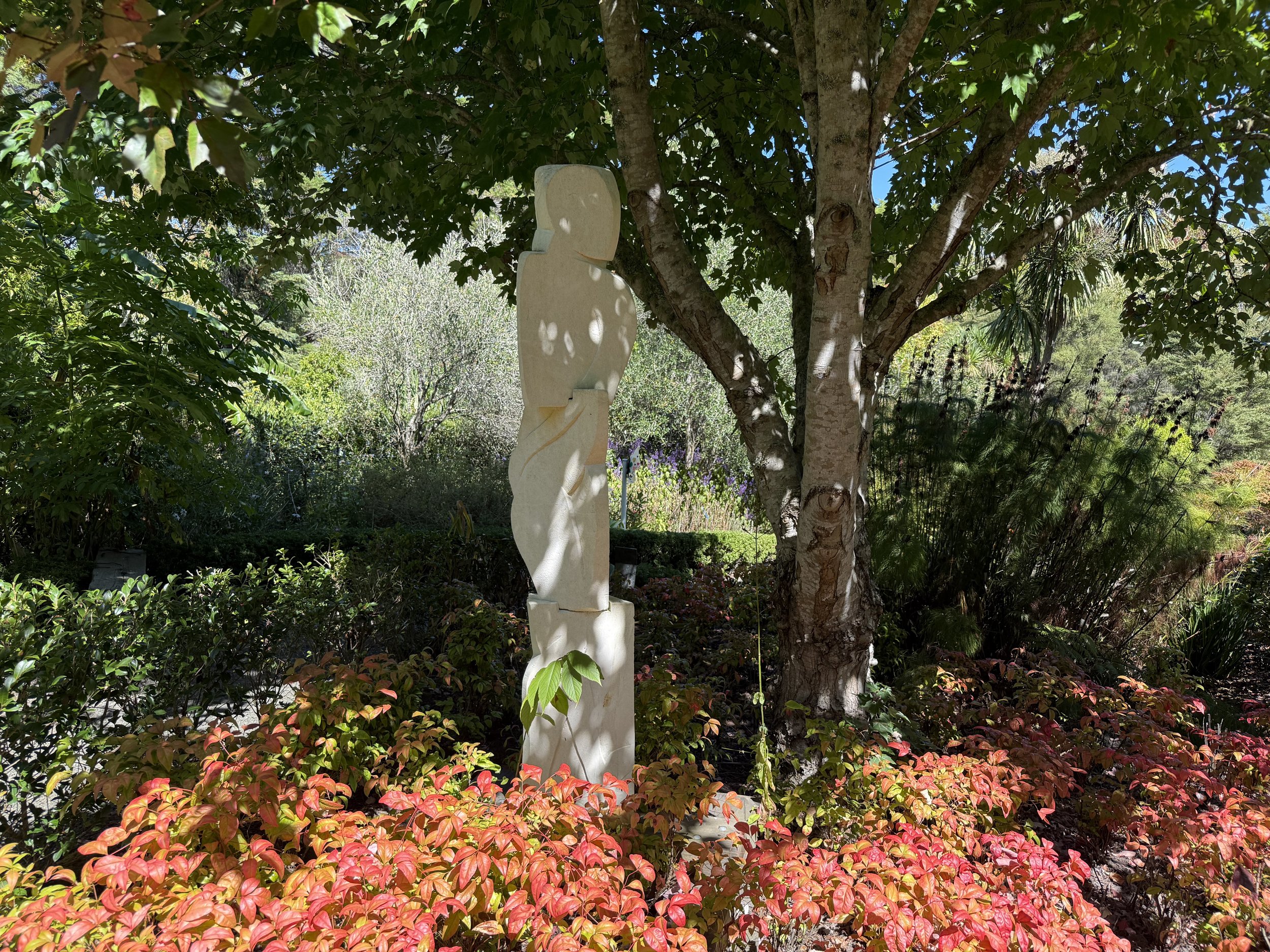 Garden with a white stone sculpture and a tree surrounded by colorful foliage.