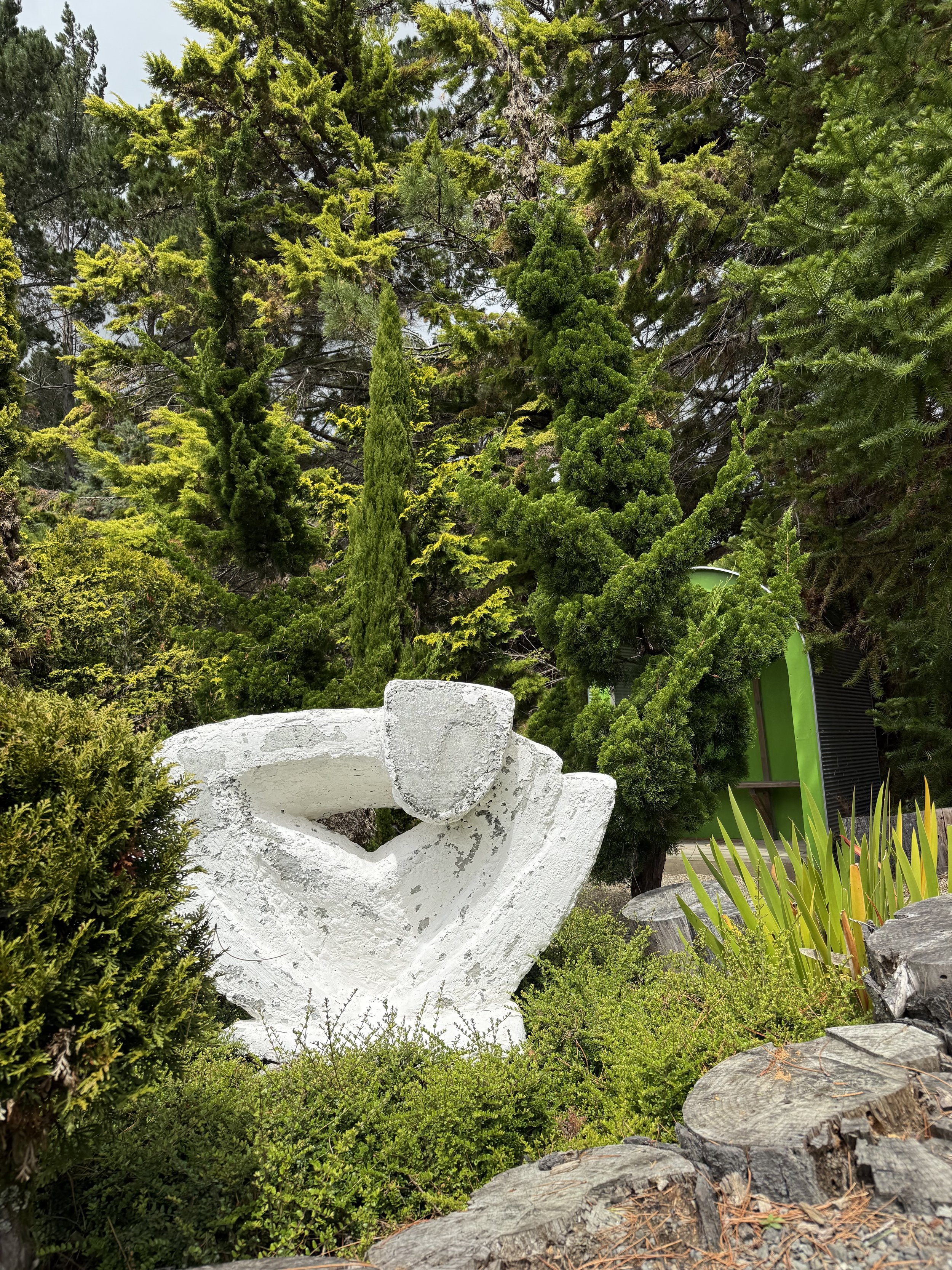 Abstract white sculpture surrounded by lush green foliage and trees.