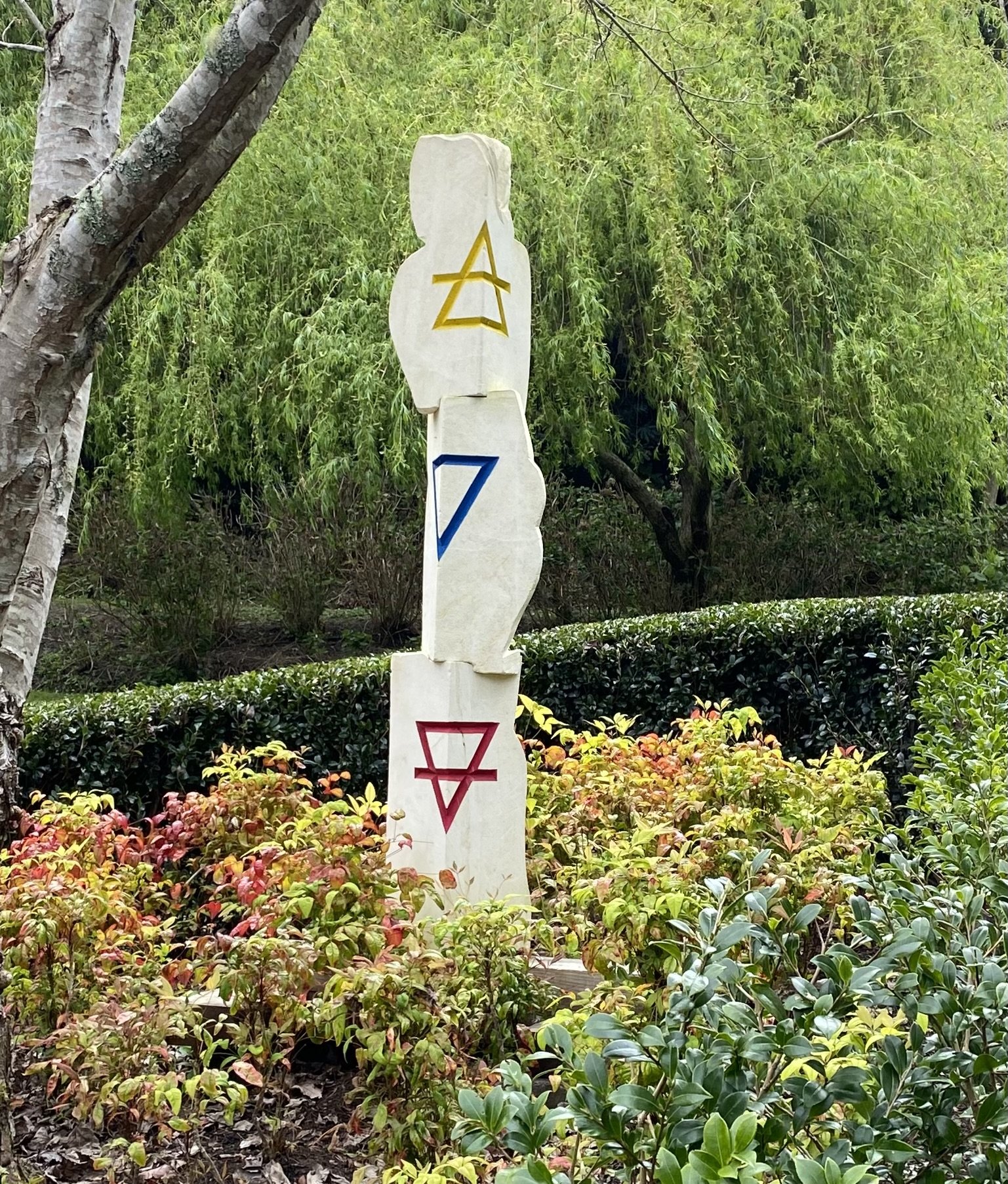 Stone sculpture with geometric symbols in a garden setting, surrounded by greenery and plants.