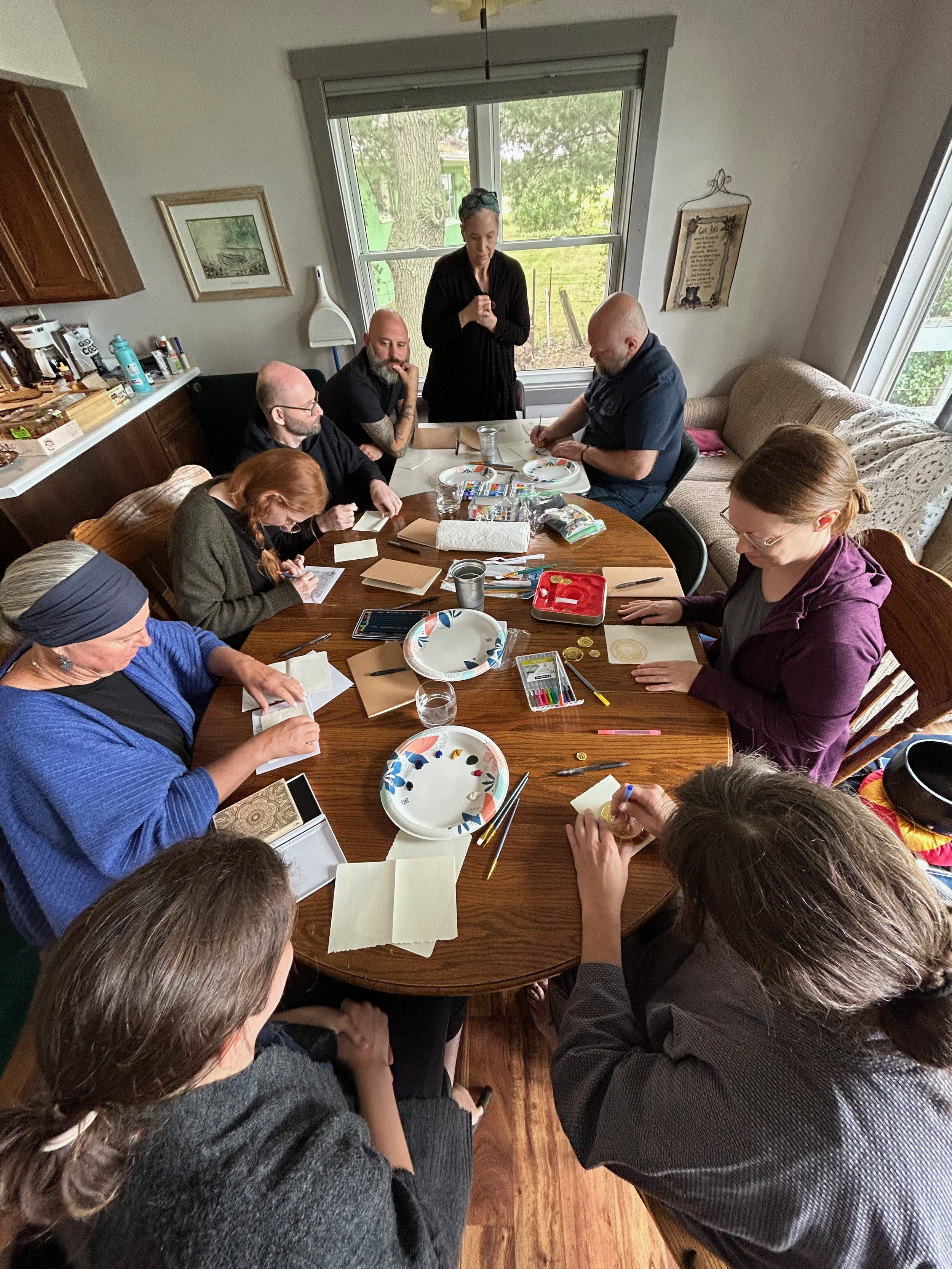 A group photo during the 2023 Minnesota Sesshin. The practitioners are gathered around a kitchen table doing a craft service project.