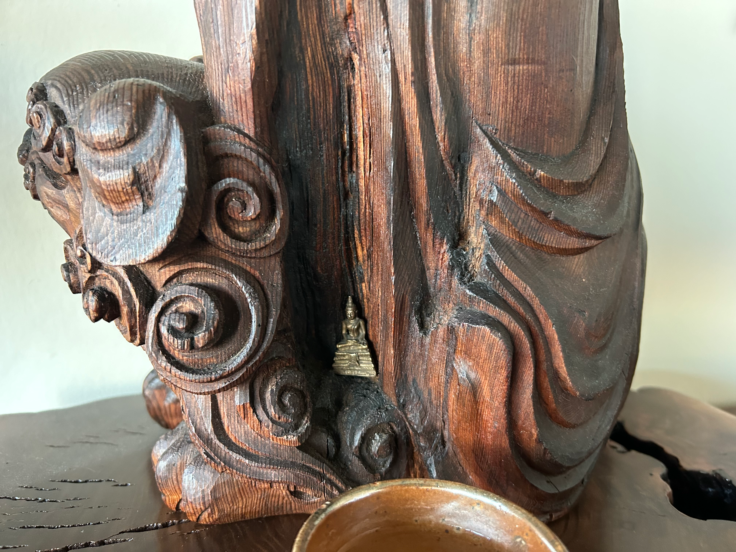 A side photo of the NBZ wooden Manjuśri statue. In one of the many folds of his robe, a small golden Buddha statue sits.