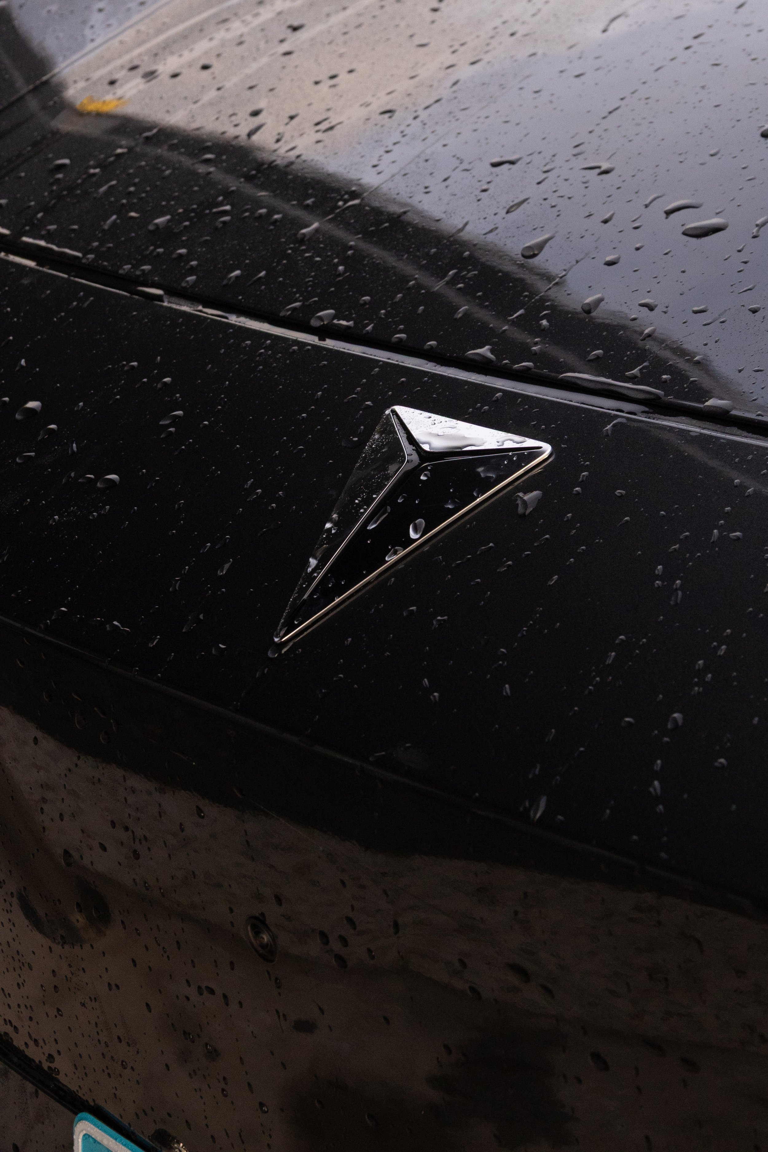 Close-up of a black car hood with water droplets and a Bonneville salt flats emblem.