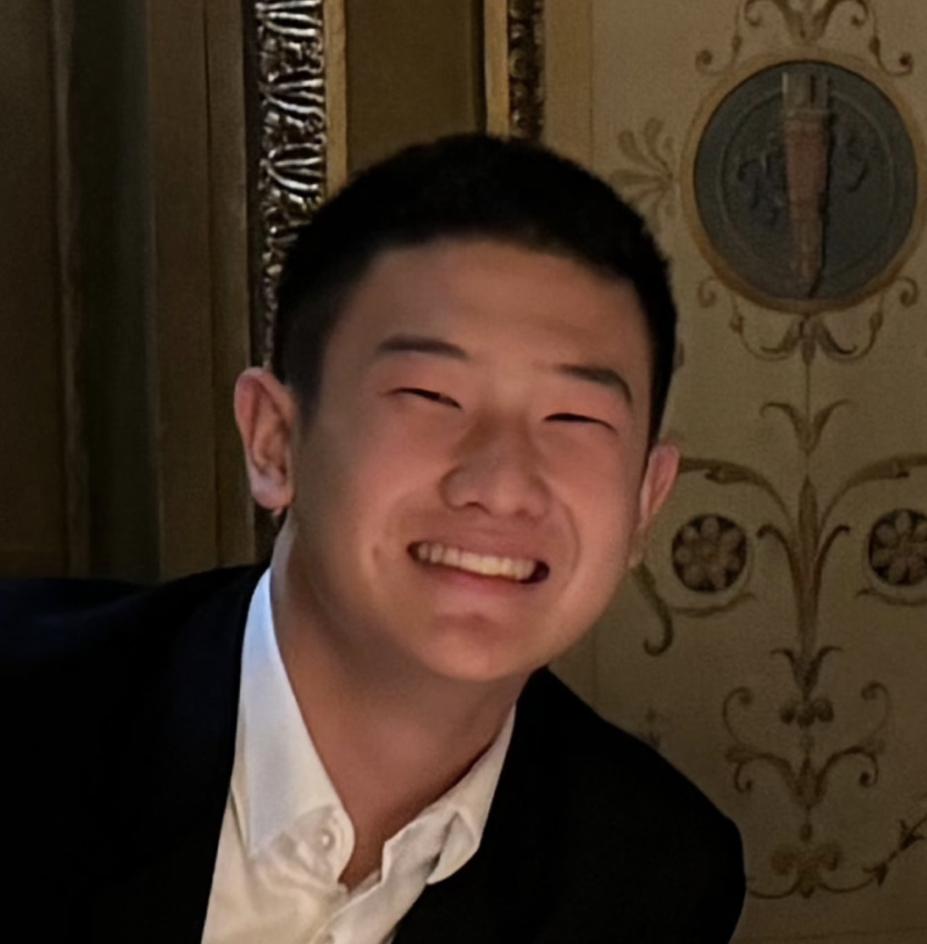Smiling person in a suit indoors with ornate wall decor.