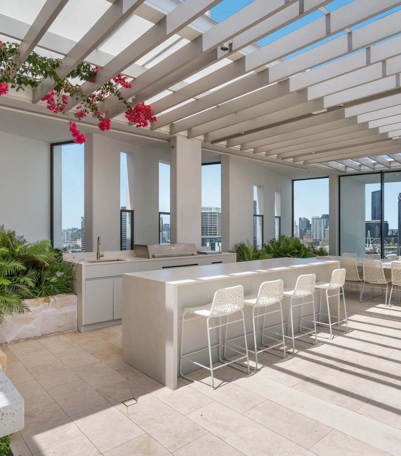 Modern rooftop outdoor area with white bar counter, chairs, plants, and Brisbane city skyline views. West End Mollison Street rooftop