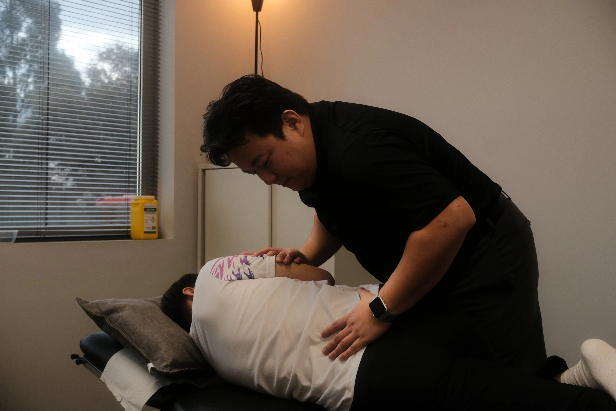 A person lying face down on a treatment table while a chiropractor performs a spinal adjustment.