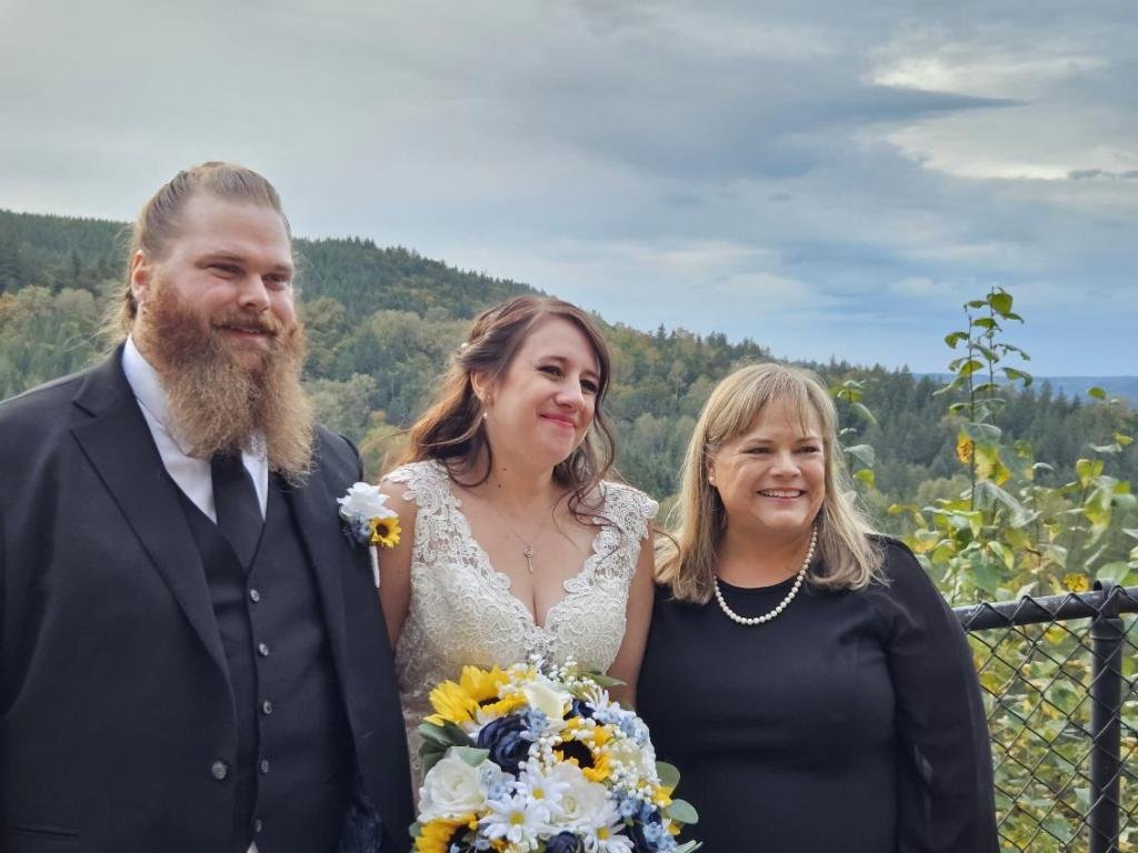 Bride and groom with a guest posing outdoors with a scenic forest view.