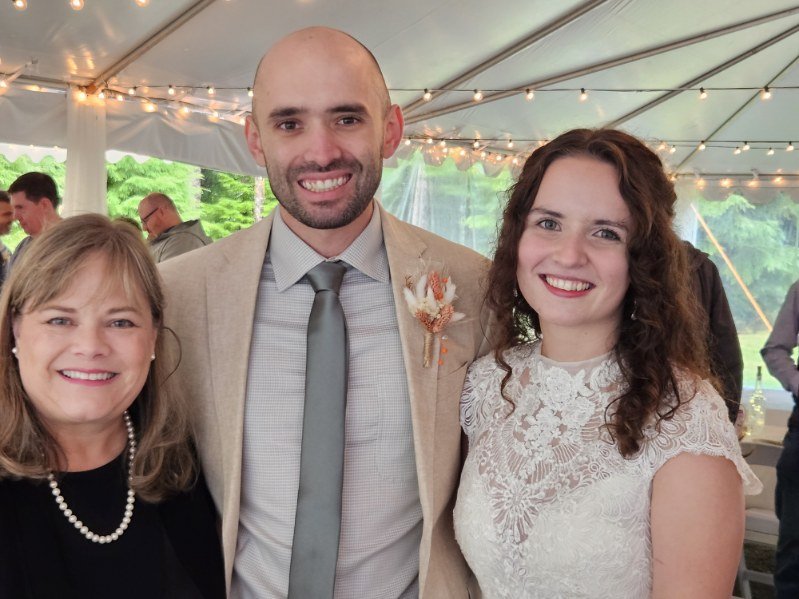 Three people smiling at a wedding reception under a tent.
