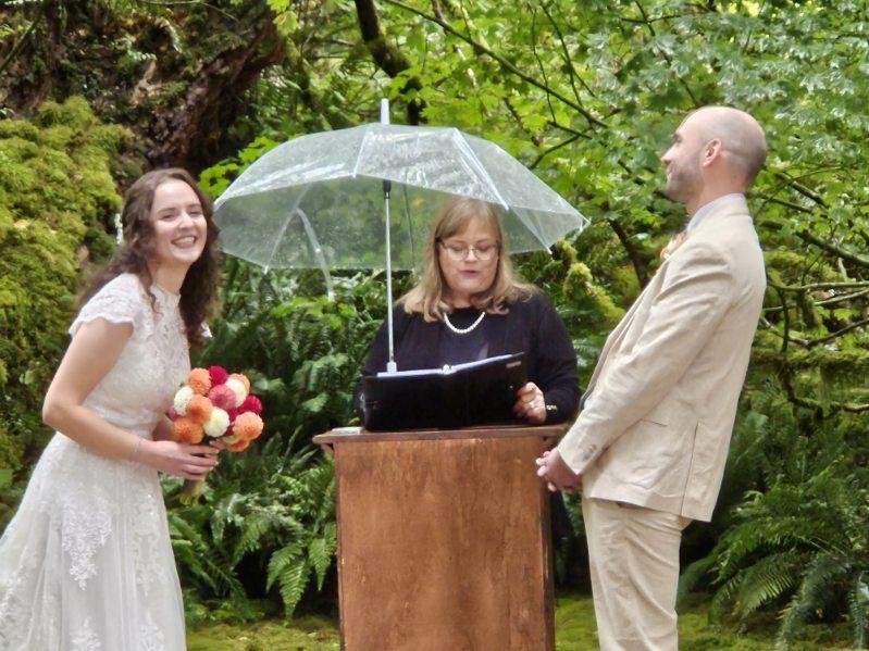 Bride and groom with officiant holding an umbrella outdoors