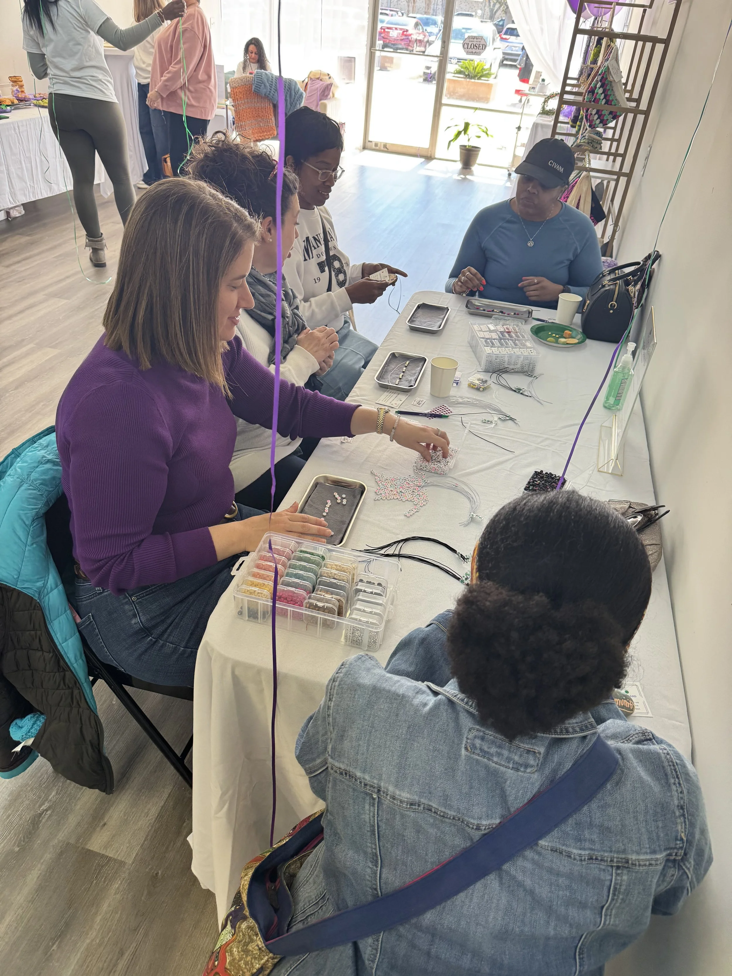 Women seated around a long table covered in beads, trays, and craft supplies during a hands-on making workshop at NaRose Designs Studio in Sugar Land, TX
