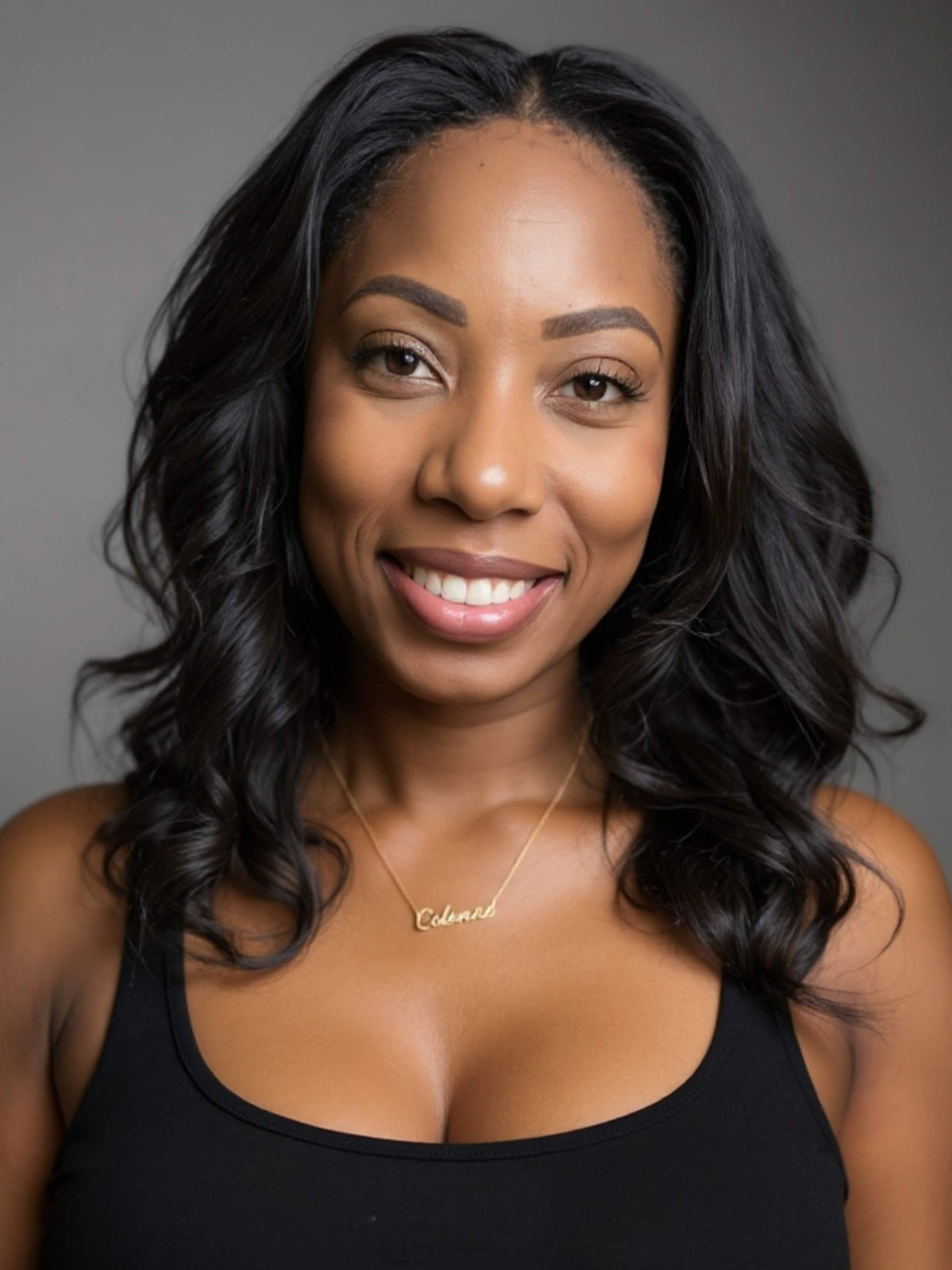 A smiling woman with black wavy hair wearing a black top and a gold necklace that says 'Celine' on a gray background.