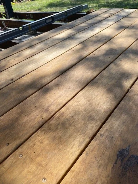 Close-up of a wooden deck under construction with evenly spaced planks and a measuring tool on top.