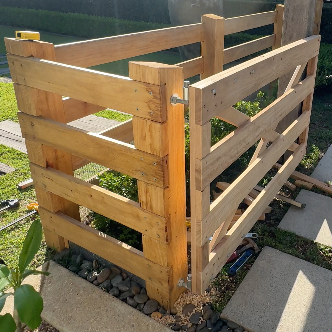 A wooden fence under construction, partially assembled with horizontal slats and vertical posts, with tools and materials nearby.
