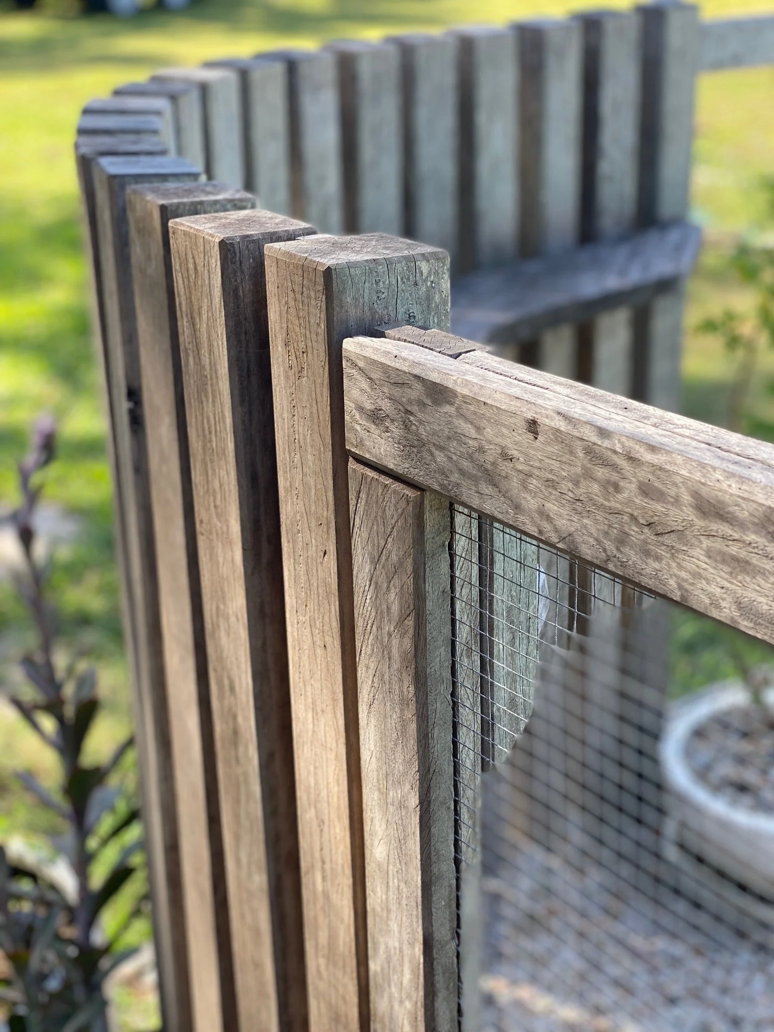 Close-up view of a wooden picket fence with a blurred background of greenery and trees.