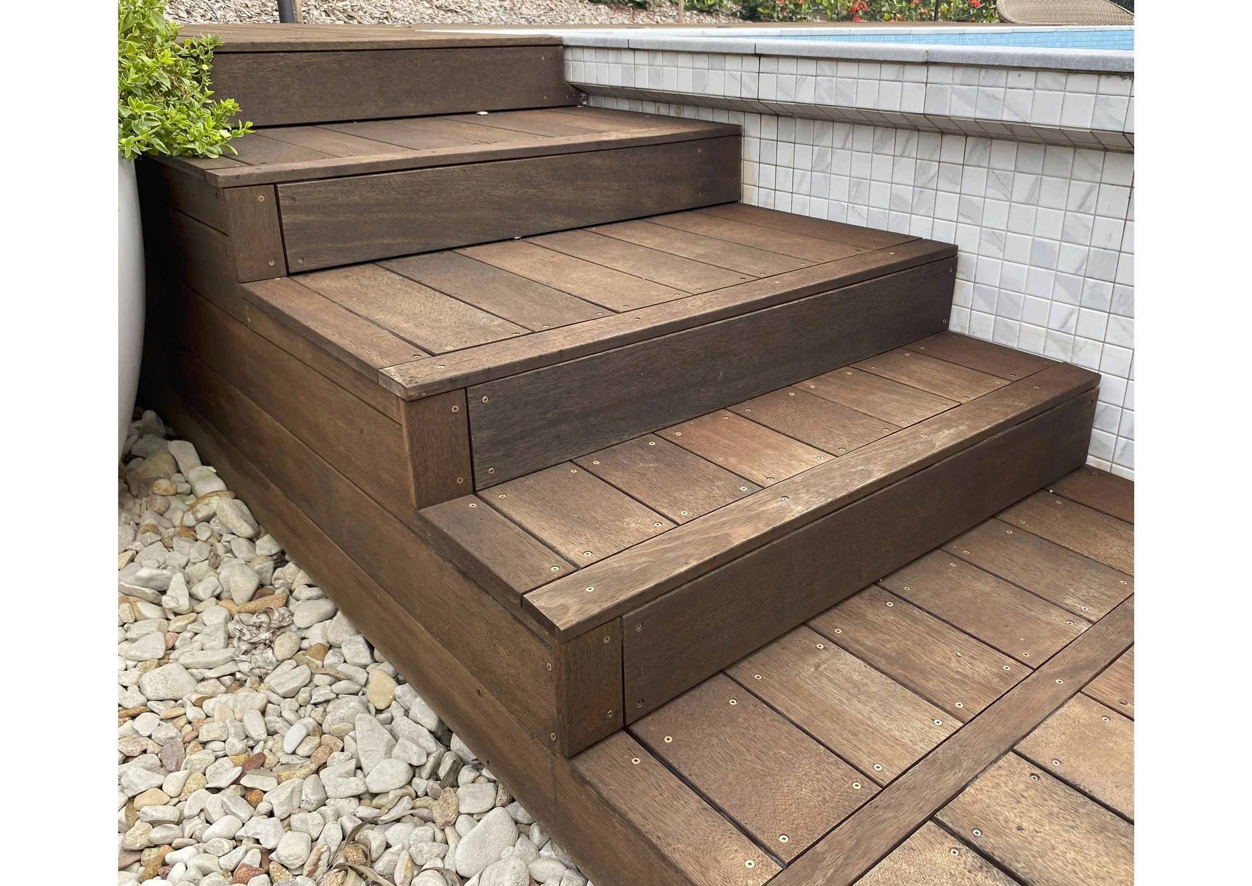 Wooden outdoor stairs leading up to a pool, with rocks on the side.