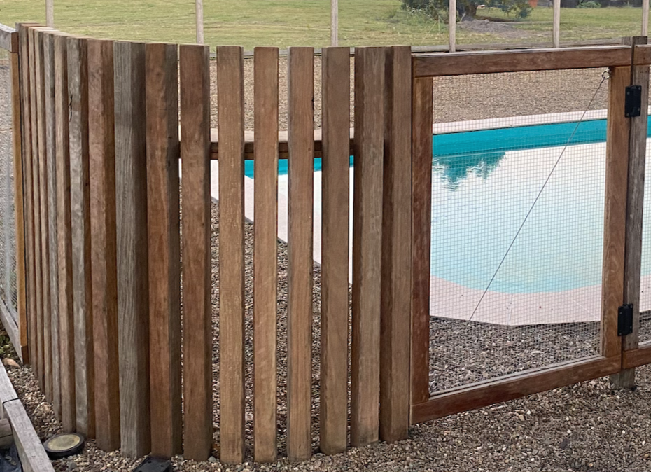 A fenced backyard pool area with wooden fencing and a gated entrance, featuring a swimming pool with a safety mesh cover.