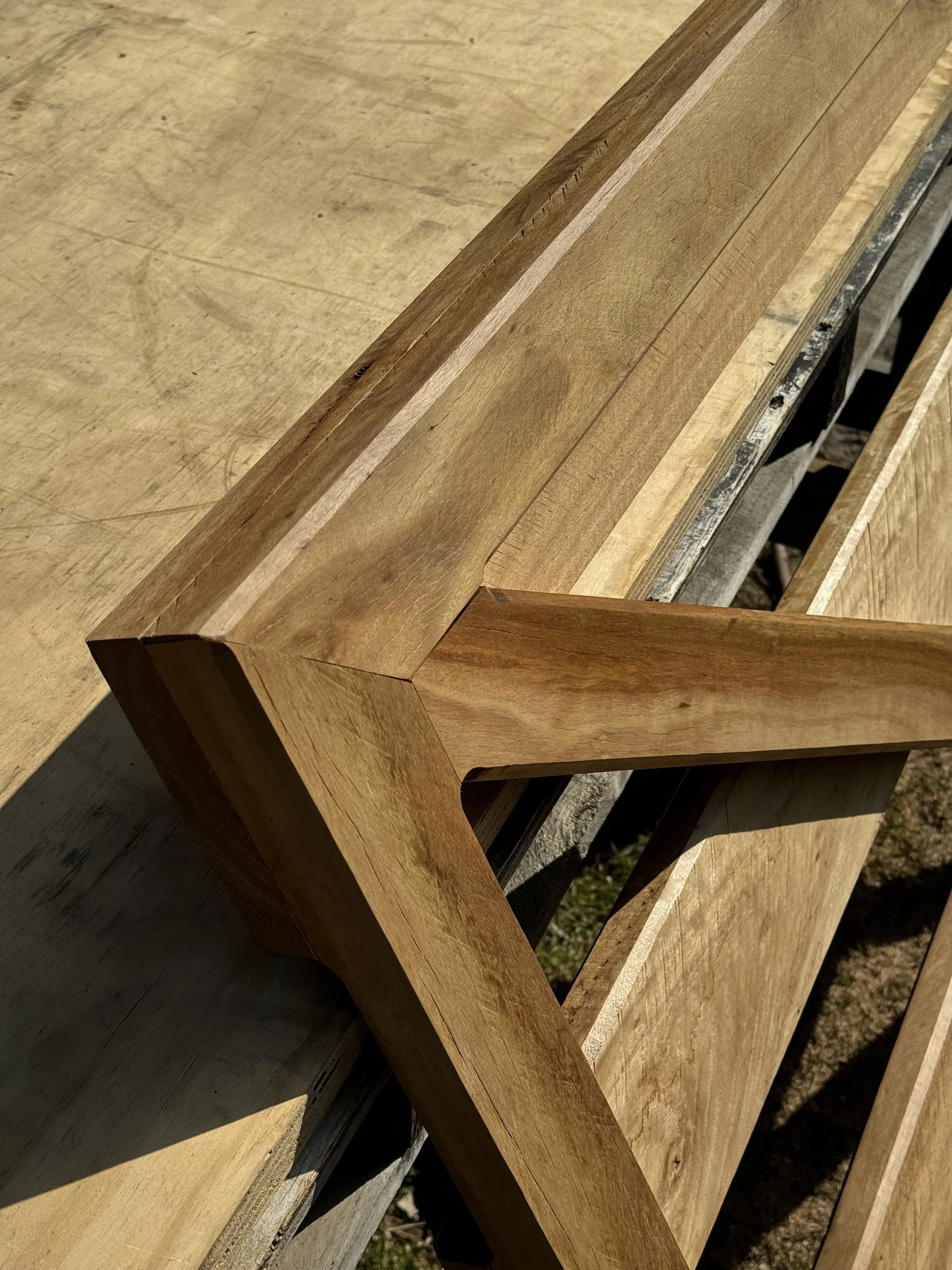 Close-up photo of a wooden furniture piece, showing detailed wood grain and corner joint, set outdoors with sunlight casting shadows.