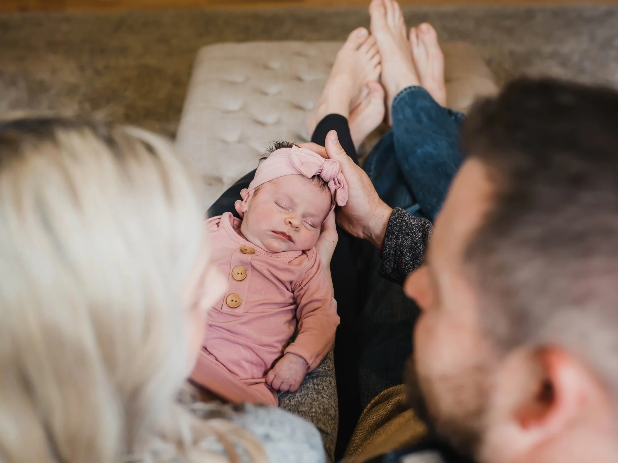 A newborn baby sleeping on a person's lap, with adults looking on lovingly, in a cozy indoor setting.