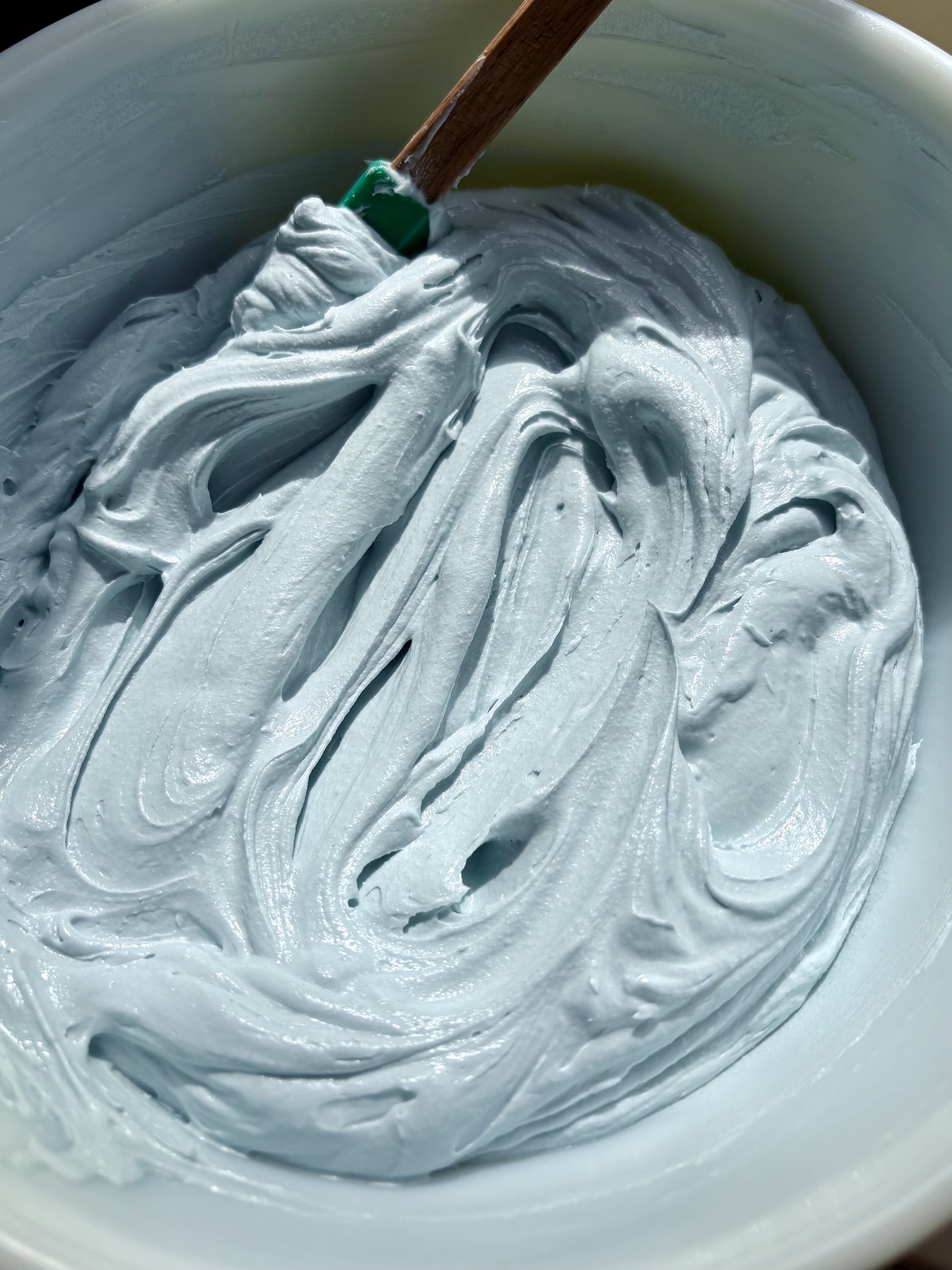 Close-up of light blue whipped cream texture in a bowl with a spatula.