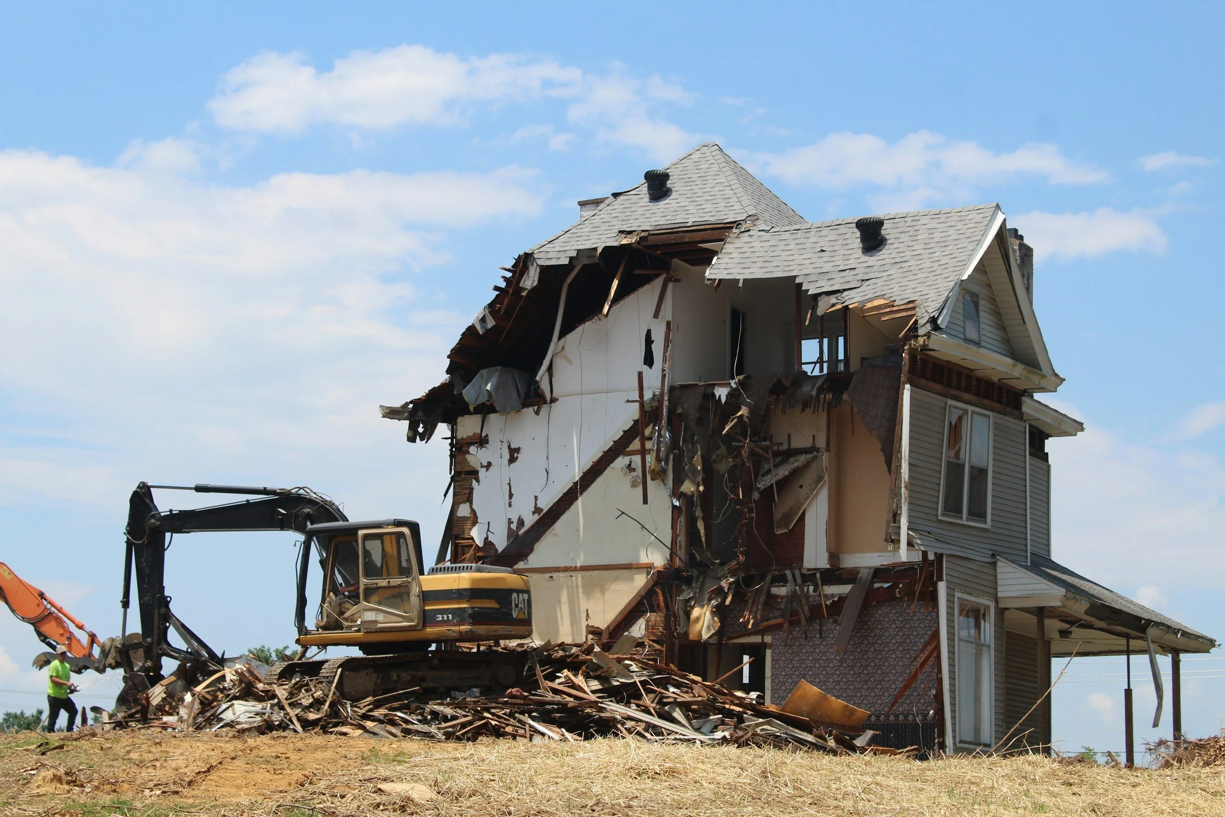 An excavator demolishing an old house, a process that requires a certified hazardous material inventory and demolition survey in Kelowna.