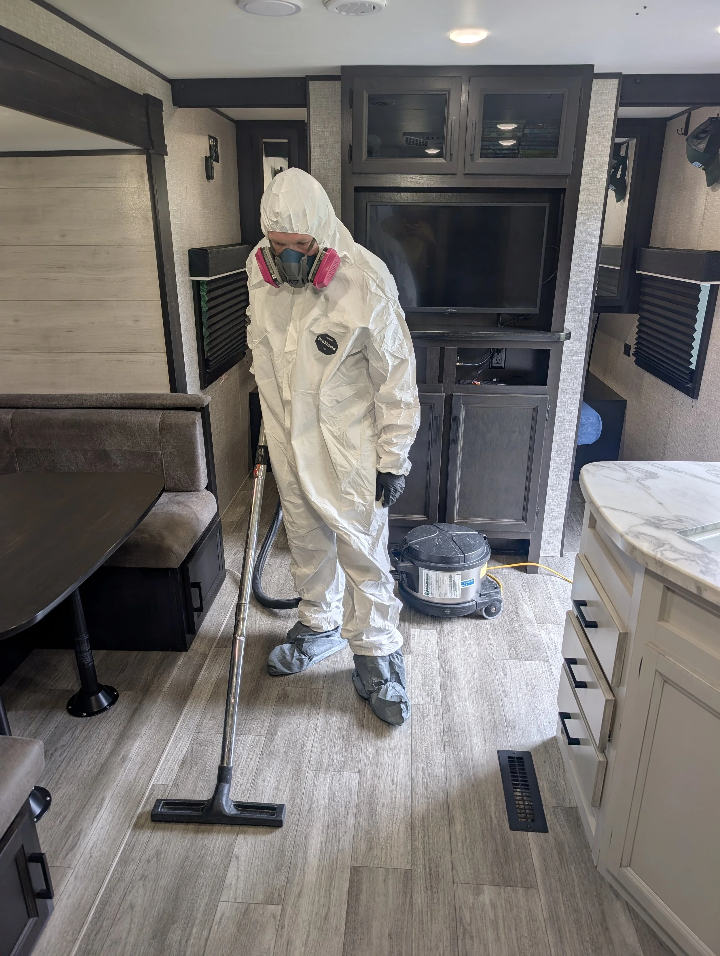 Certified hazard abatement specialist using an industrial HEPA vacuum for safe rodent waste removal in an Okanagan camper.