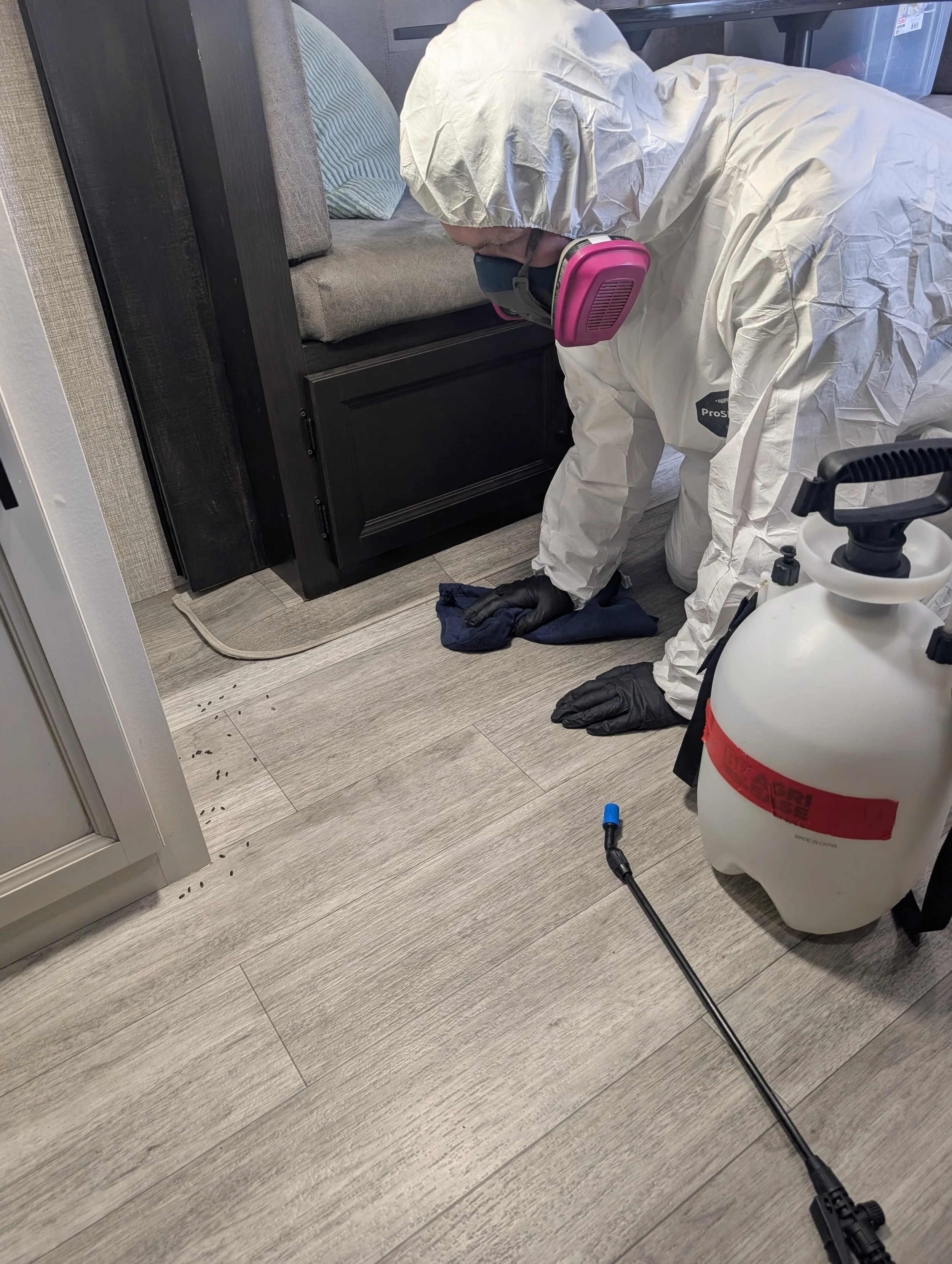 Certified technician in full PPE applying child and pet-safe disinfectant to an RV floor in Kelowna, BC.
