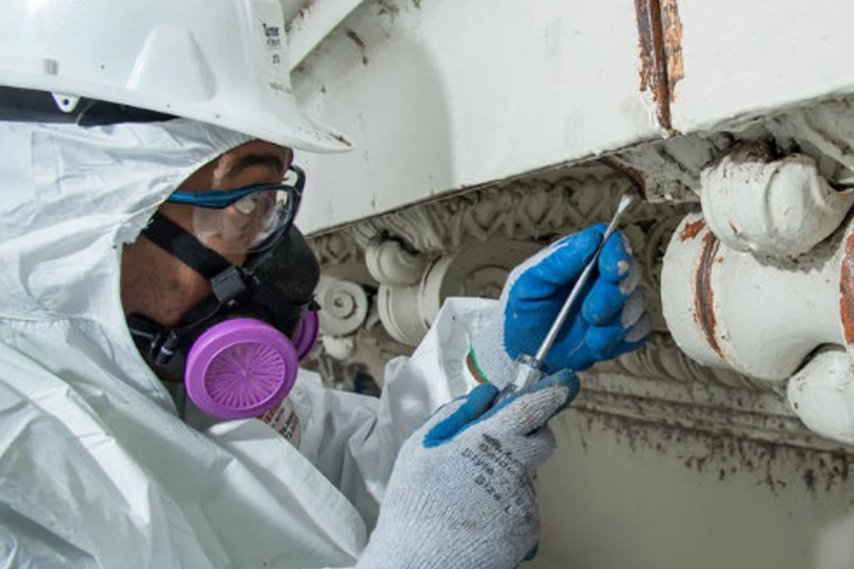 Interior Abatement technician in professional PPE taking a representative drywall sample for asbestos testing in a Vernon home.