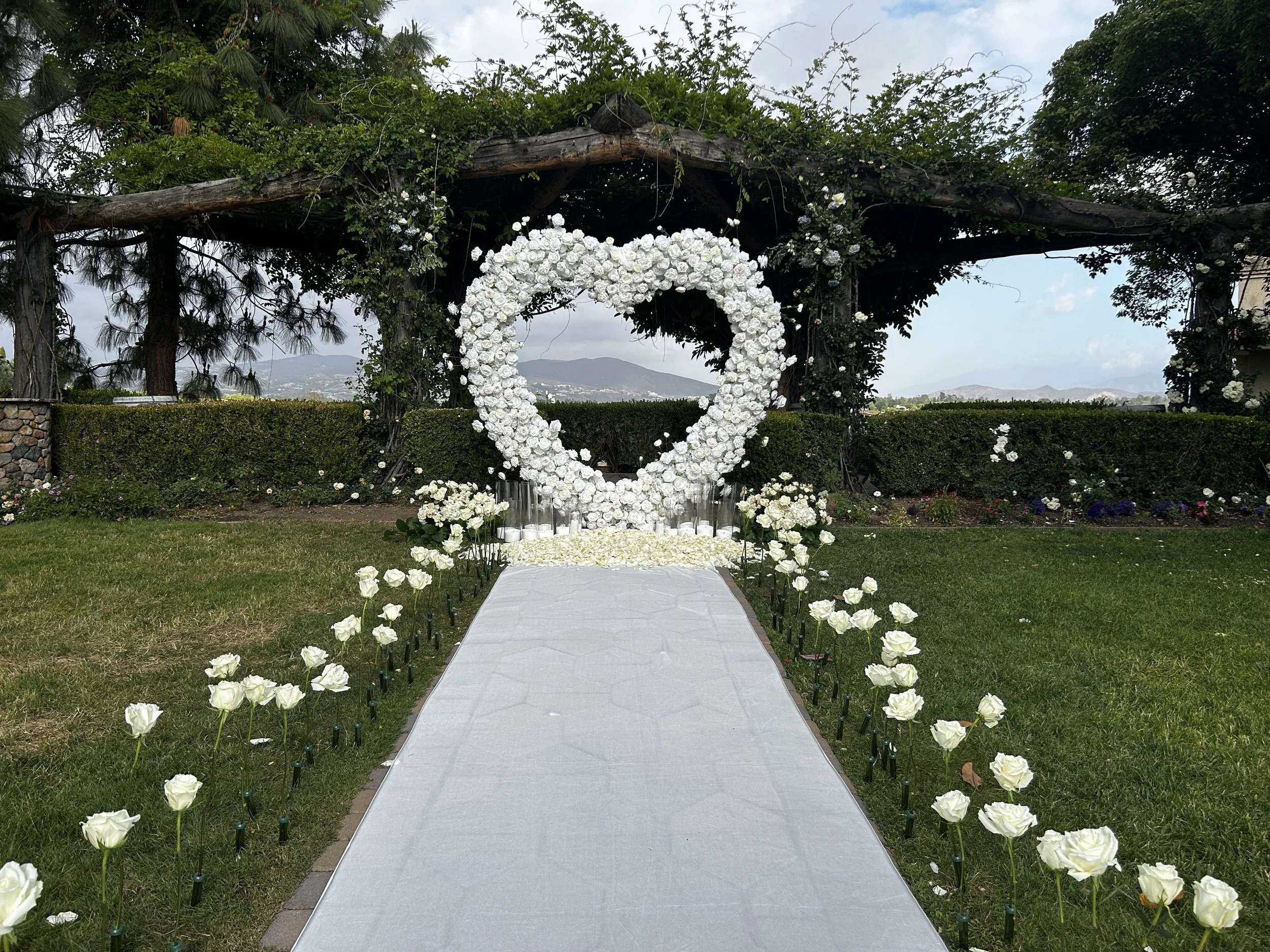 White floral heart arch with candlelight and standing rose aisle in front of an arbor with mountain views