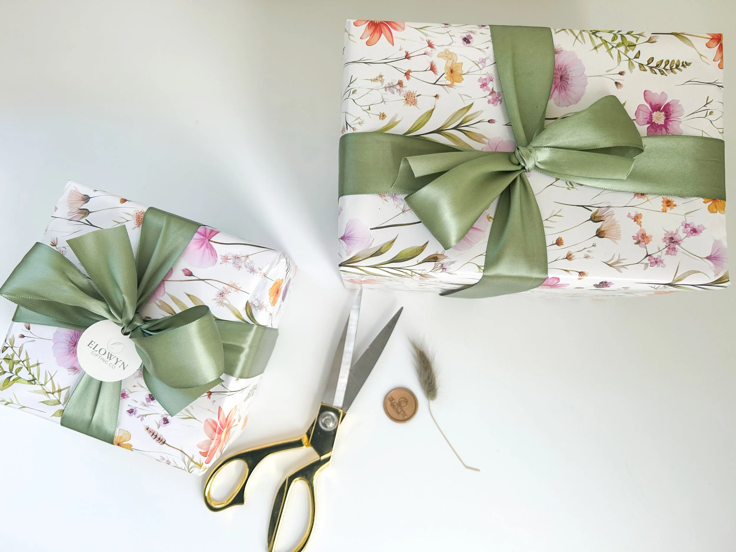 Two wrapped gifts with floral and white paper green satin ribbon gift tags gold scissors a wax seal and bunny tail enhancement