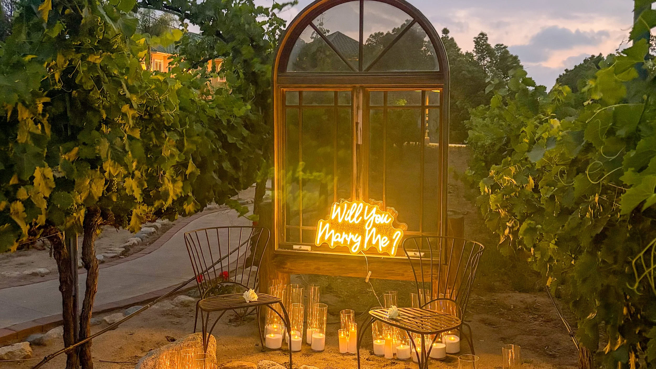 Candlelight proposal moment among wines with a neon sign sitting on a window sill with two chairs