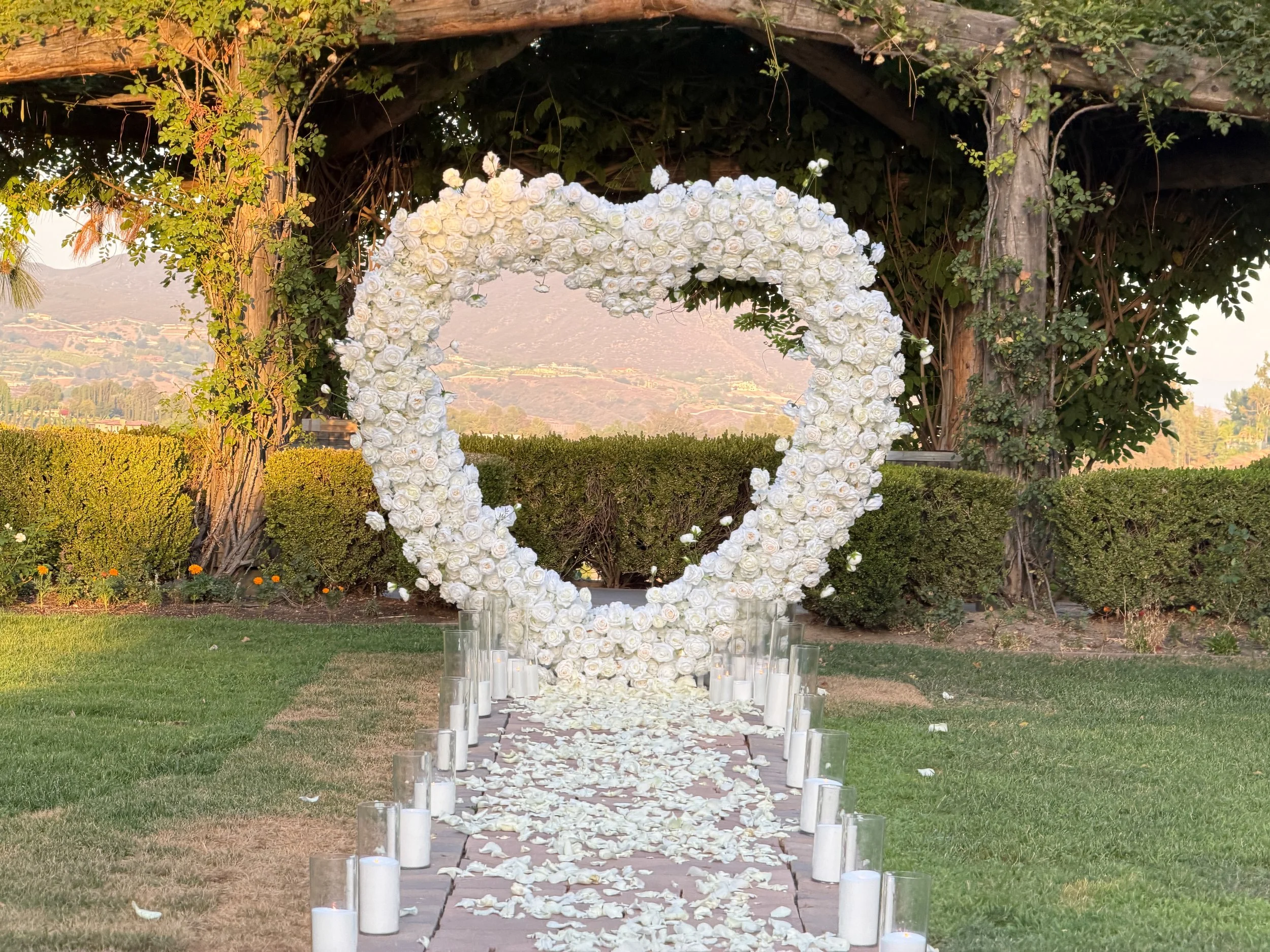 White floral heart arch with candlelight and standing rose aisle in front of an arbor with mountain views