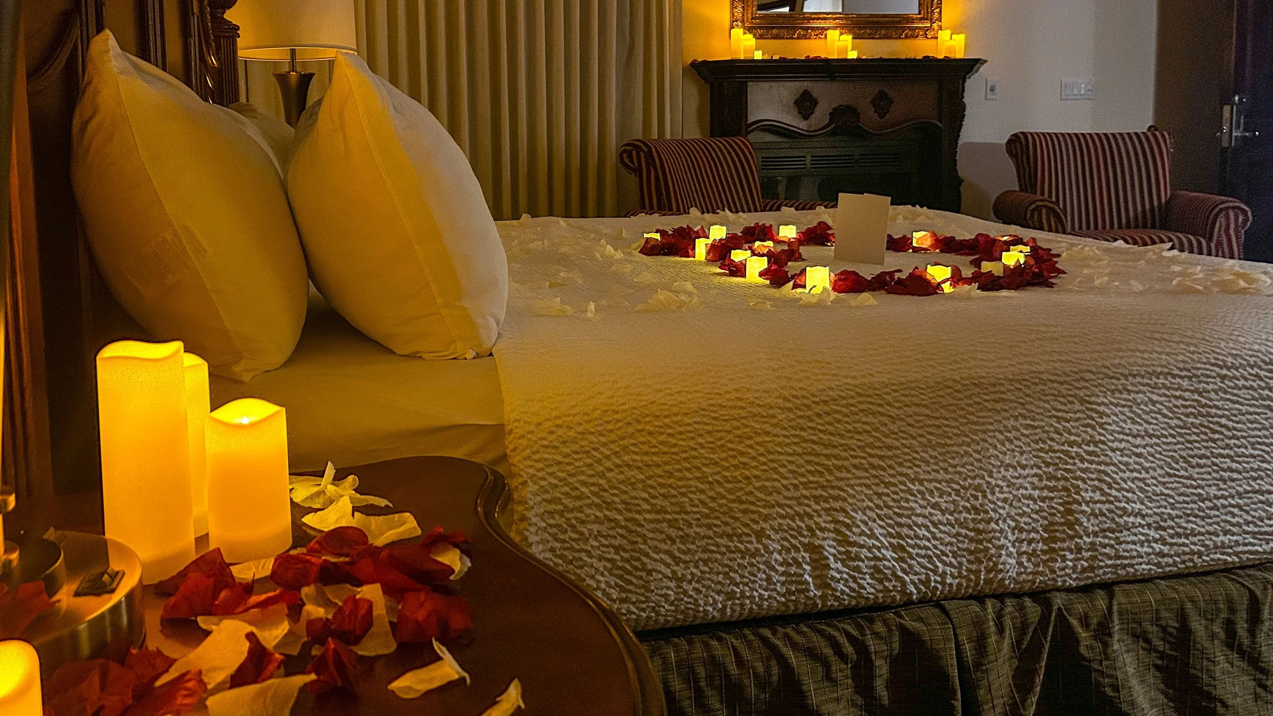 hotel room bed with a rose petal heart on a bed candle light a fire place 