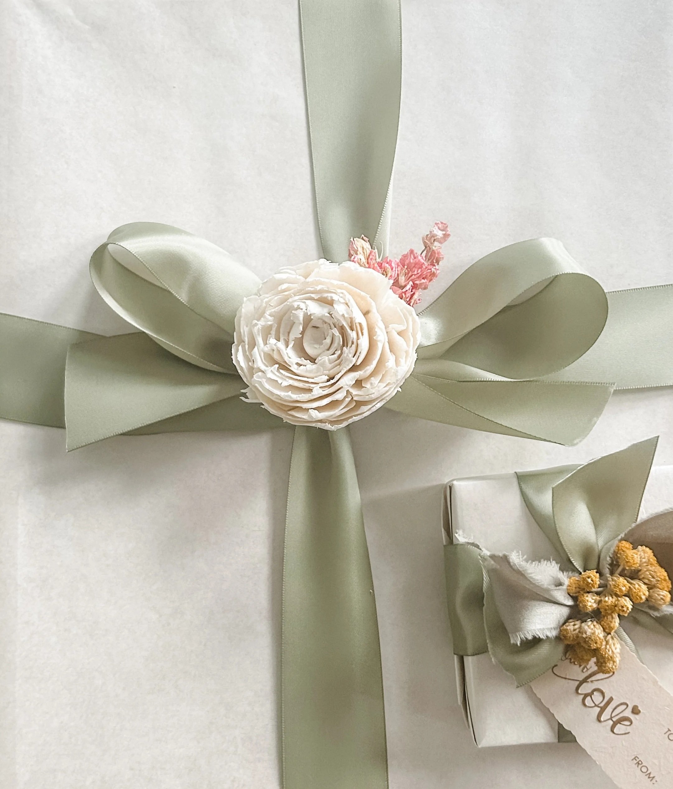 Two wrapped gifts in white paper with sage ribbons with dried florals added to the ribbon