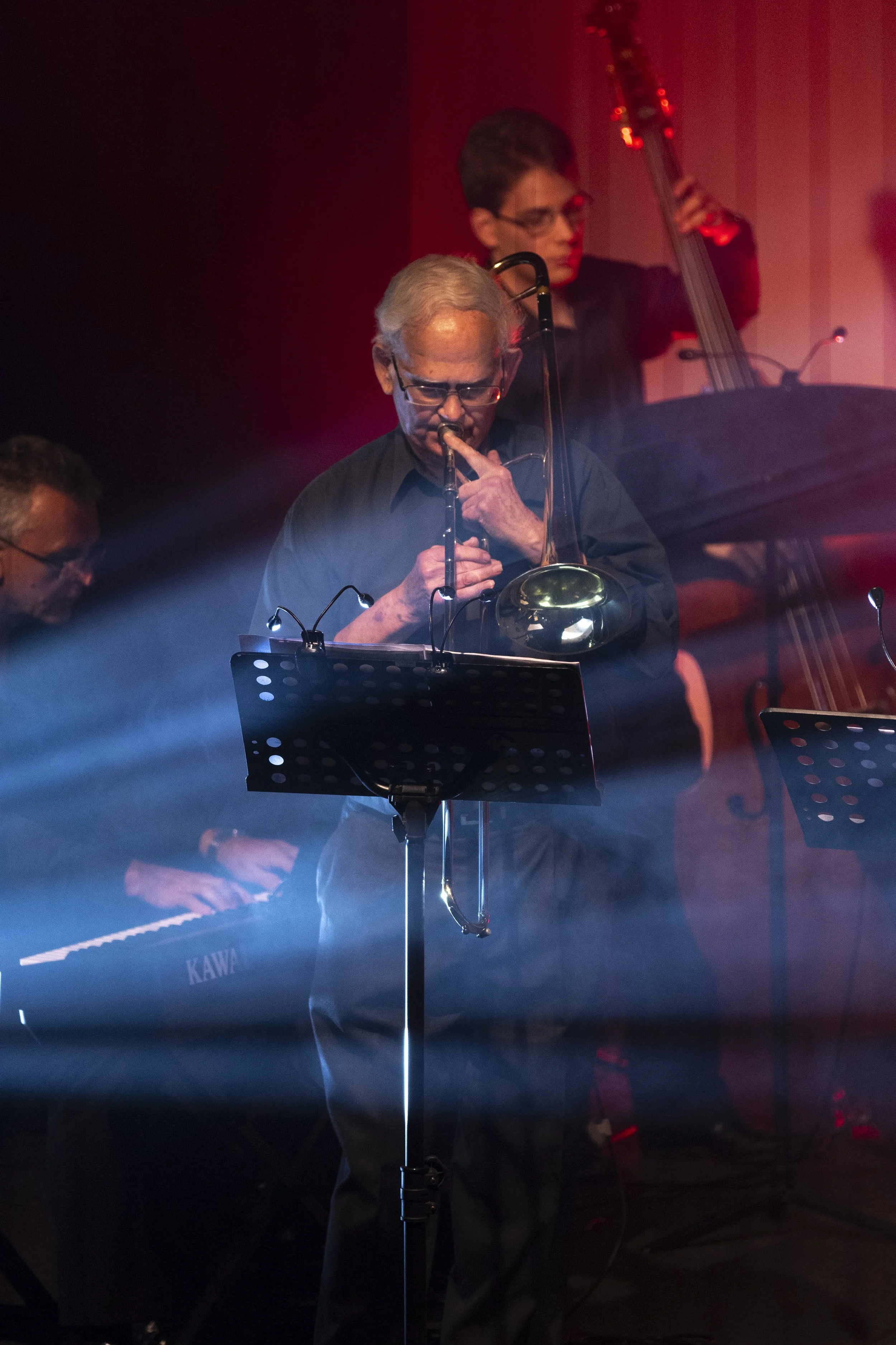 Musicians performing on stage with a trombone and keyboard under stage lights.