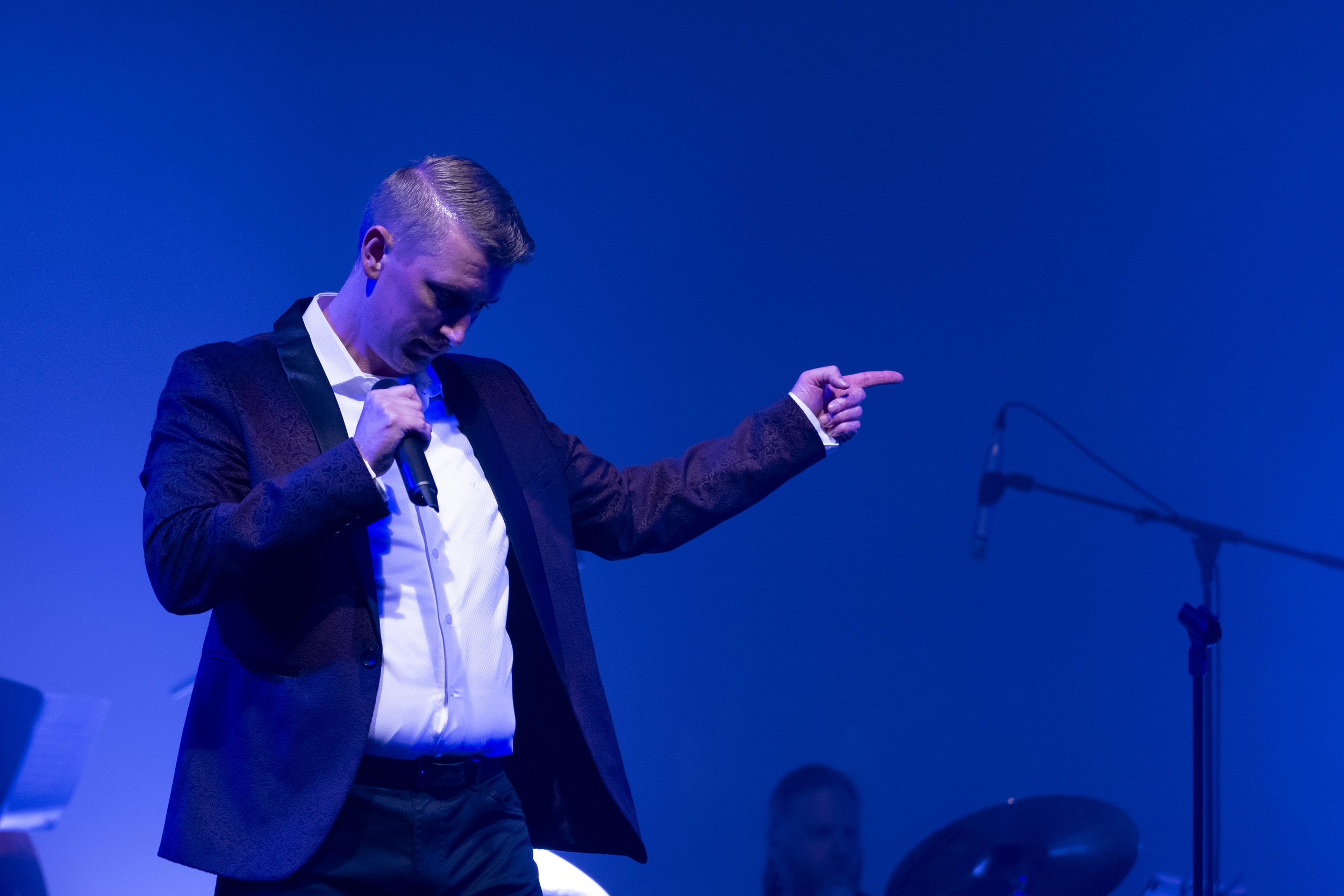 Singer in suit holding a microphone on stage with blue lighting
