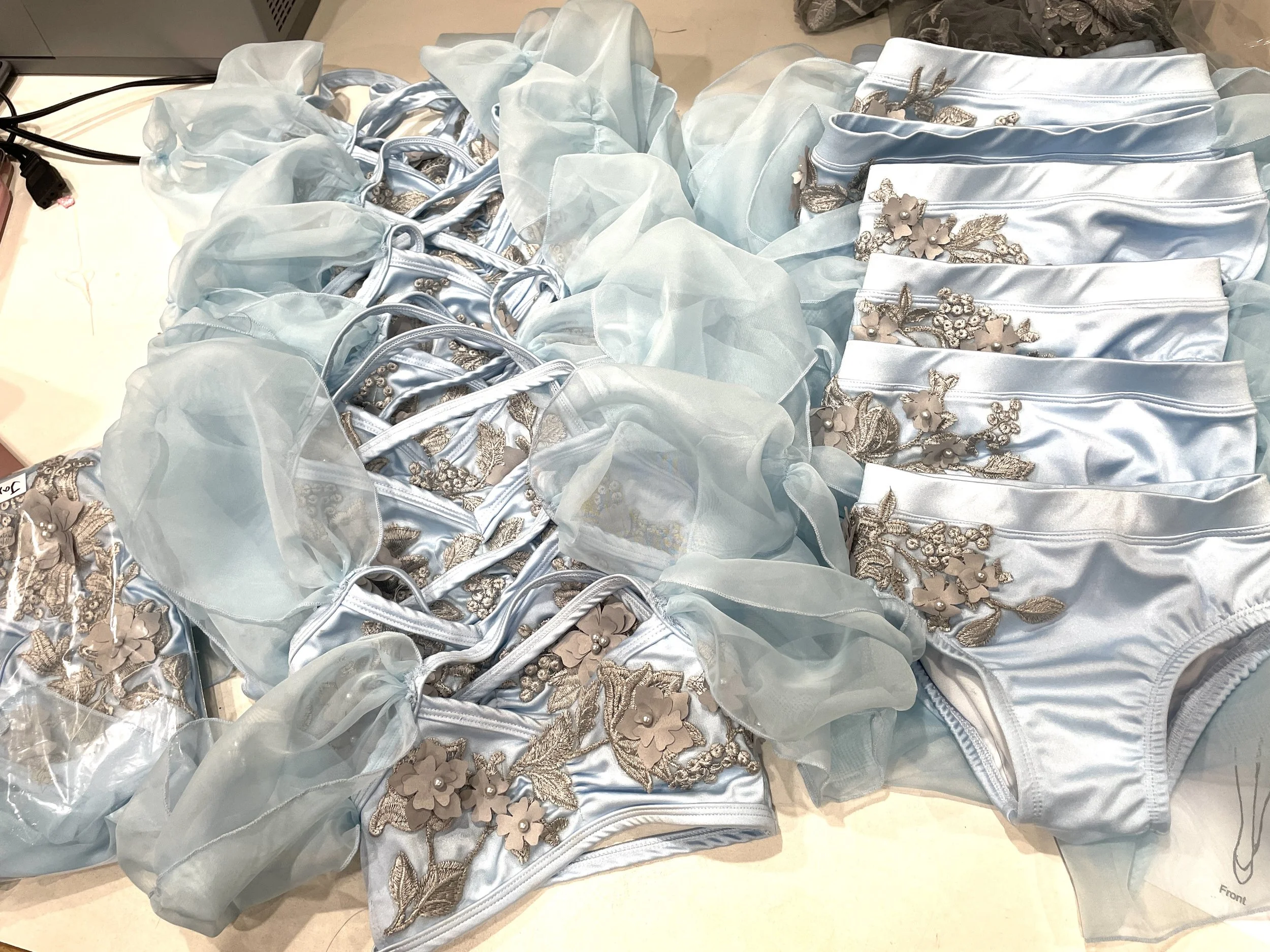 Multiple light blue satin and chiffon skirts or dresses with floral embellishments laid out on a table.