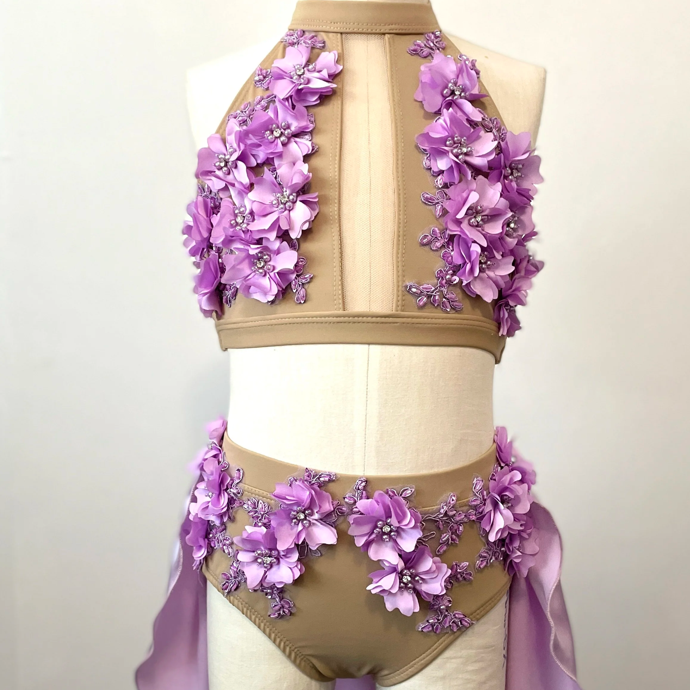 Beige mannequin wearing a two-piece outfit with lavender 3D floral appliqué, including a sleeveless top and matching shorts with lavender ribbons.