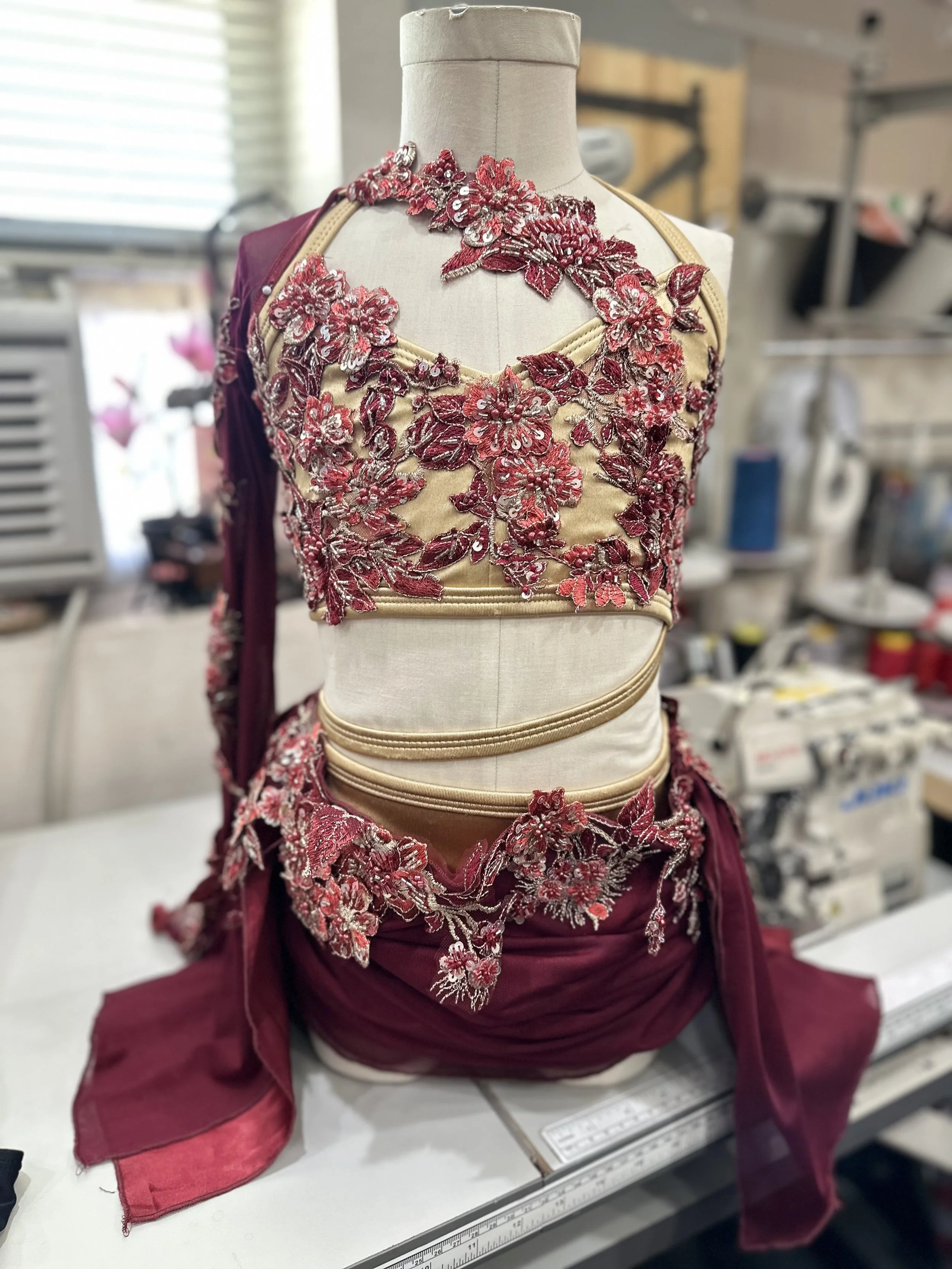 A mannequin wearing a maroon and beige traditional garment with intricate floral embroidery and embellishments.