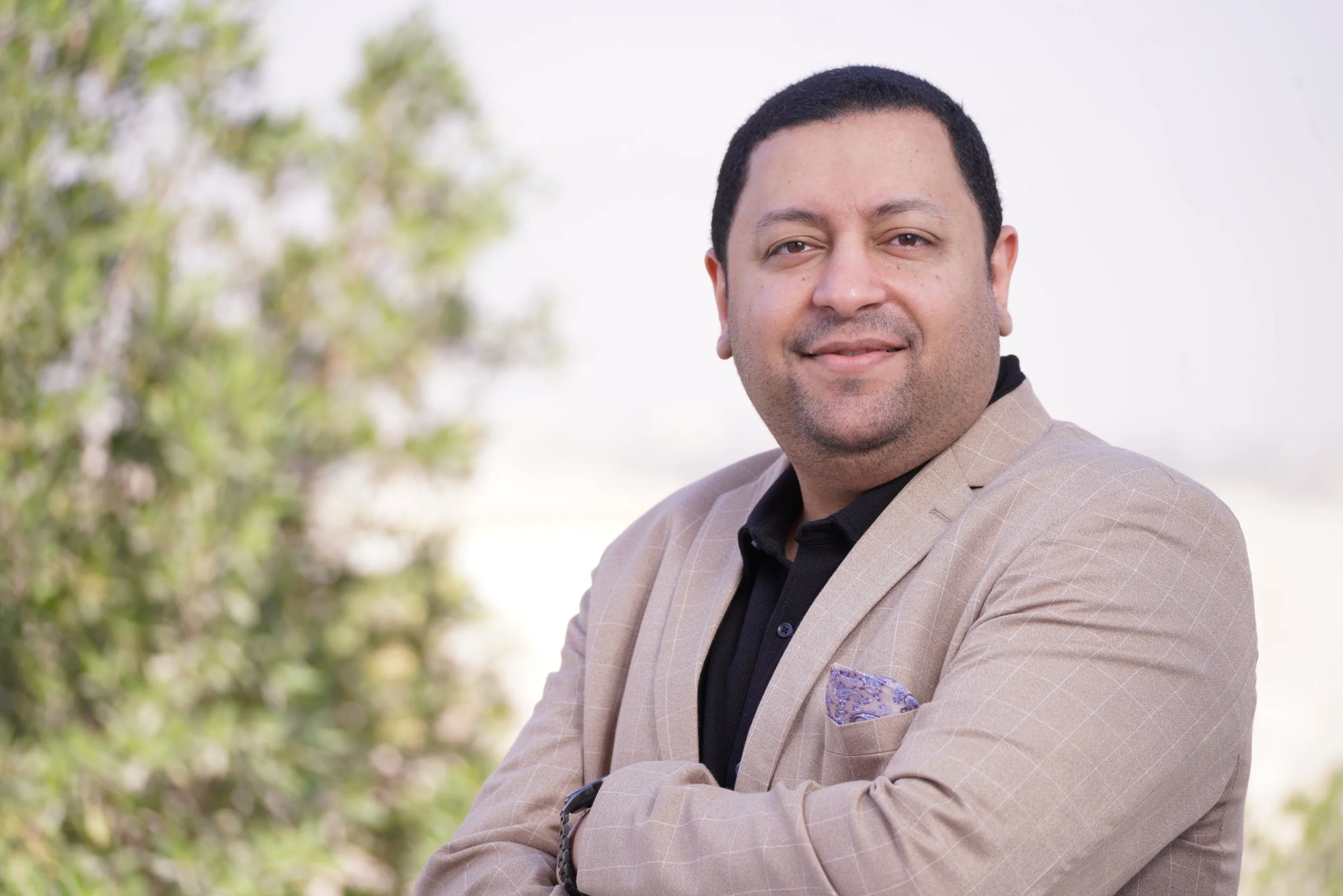 Portrait of a man with short dark hair and a beard, wearing a black jacket and striped shirt against a plain background.