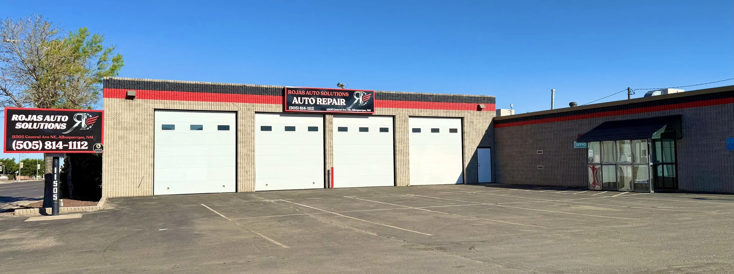 Exterior of Rojas Auto Solutions auto repair shop with three garage doors, a sign with the business name, and a parking lot.