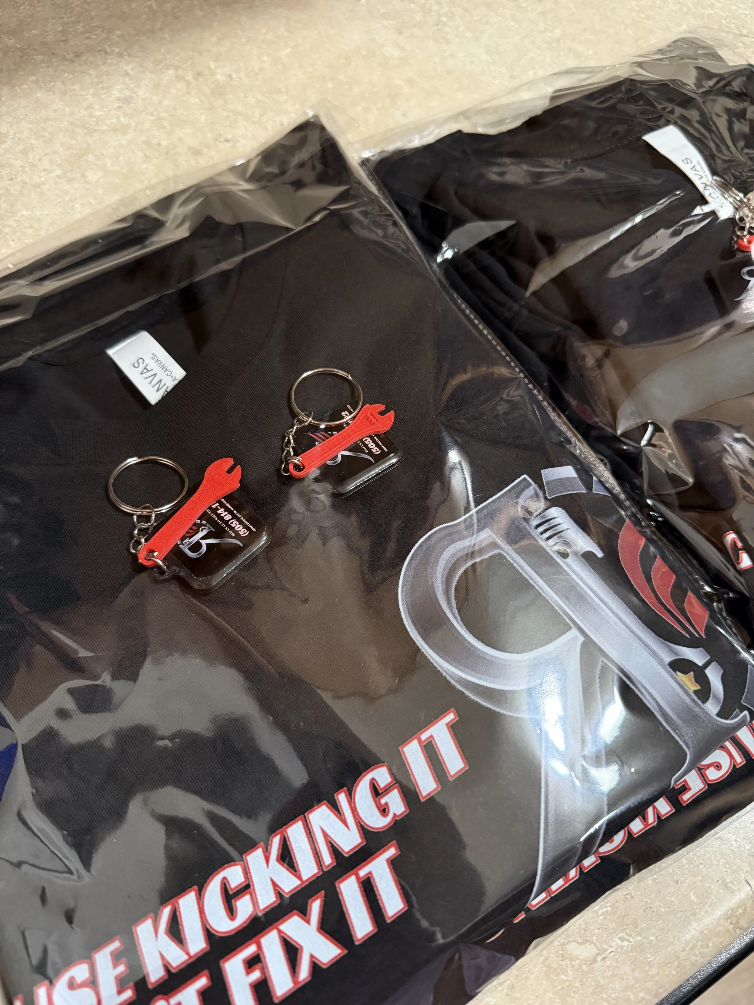 Clear plastic packaging with a black sticker that reads 'FLEXfix' in red and white letters. Inside the packaging are small keychains or charms, each with a red tool-shaped decoration and a black rectangular tag.
