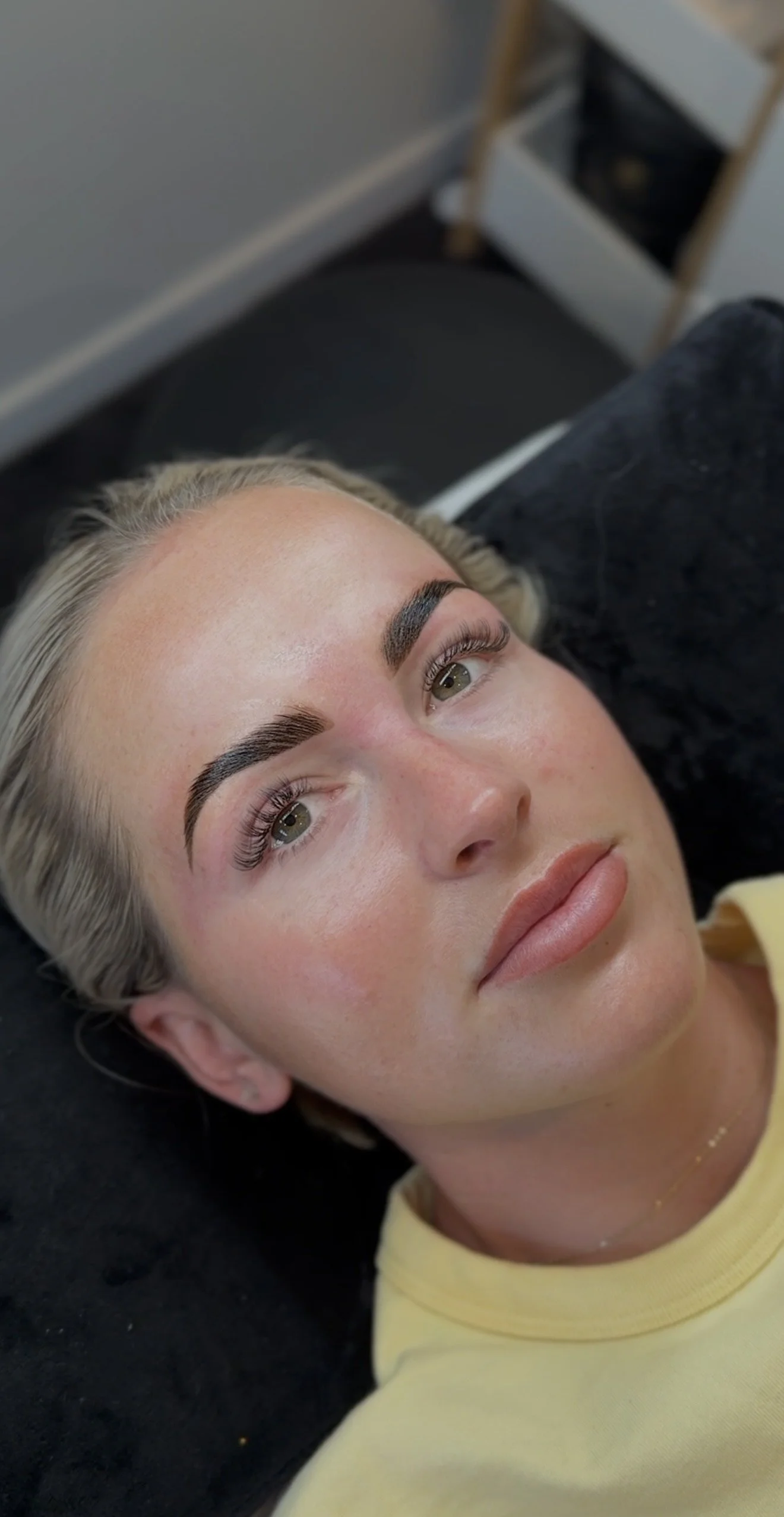 Person with styled eyebrows and natural makeup lying on a black cushion.