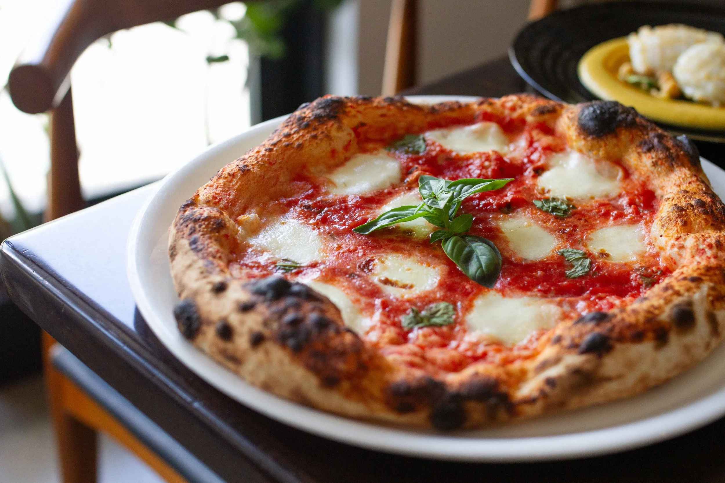 A Margherita pizza with basil leaves, melted mozzarella cheese, tomato sauce, and a crispy crust on a white plate.