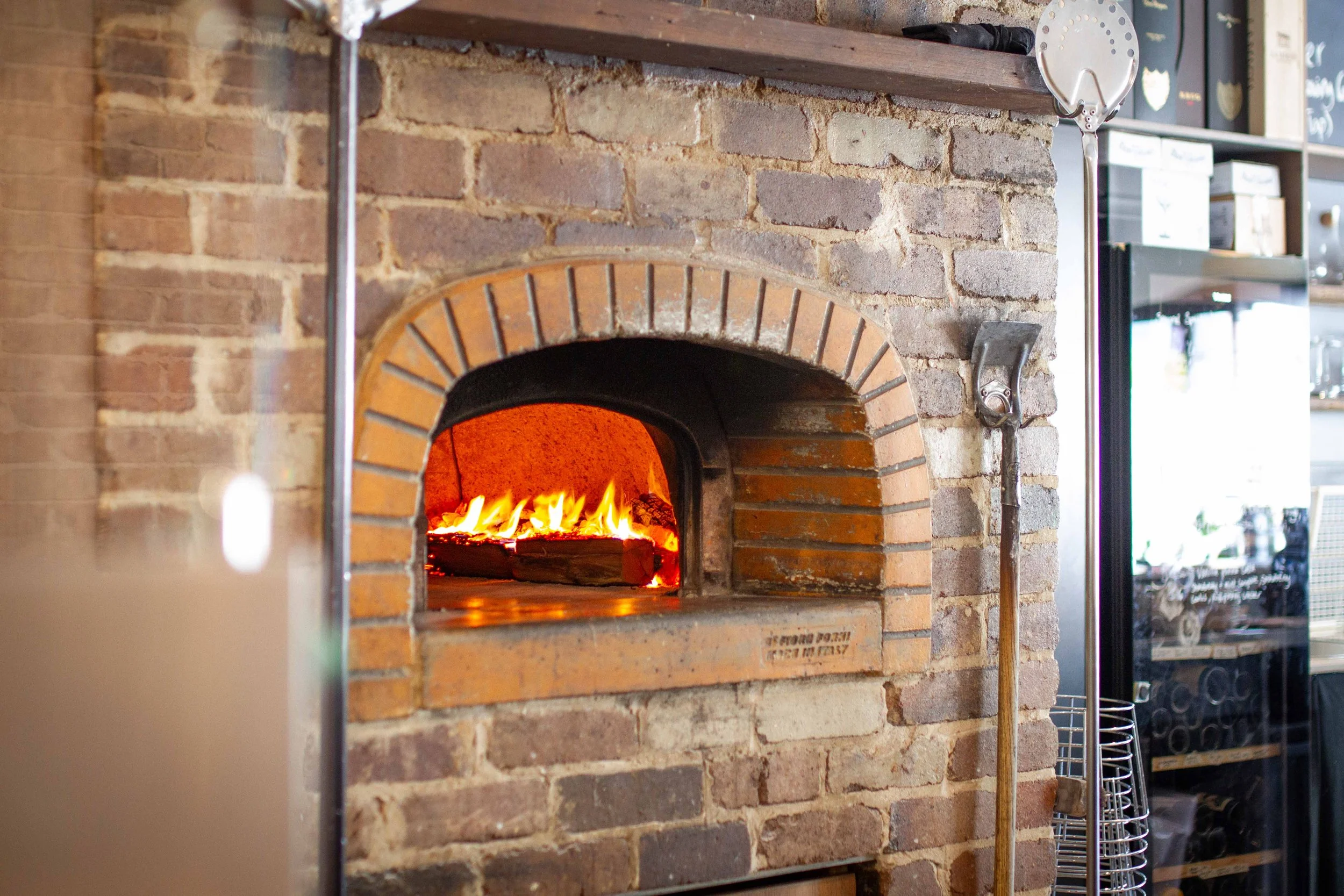 Brick pizza oven with fire inside, located in a restaurant kitchen or bakery.