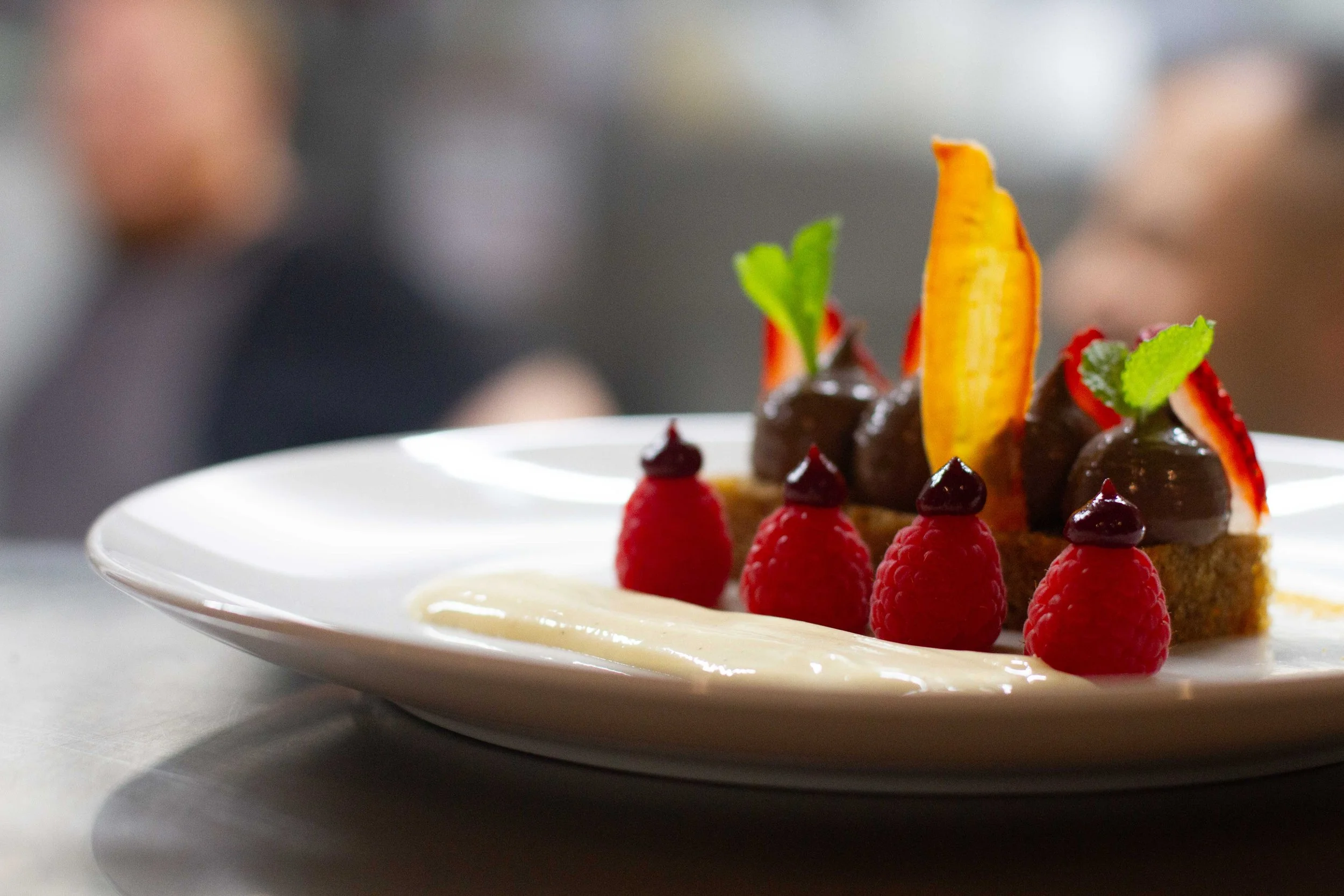 Dessert plate with raspberries, strawberries, chocolate-covered profiteroles, and garnishes.